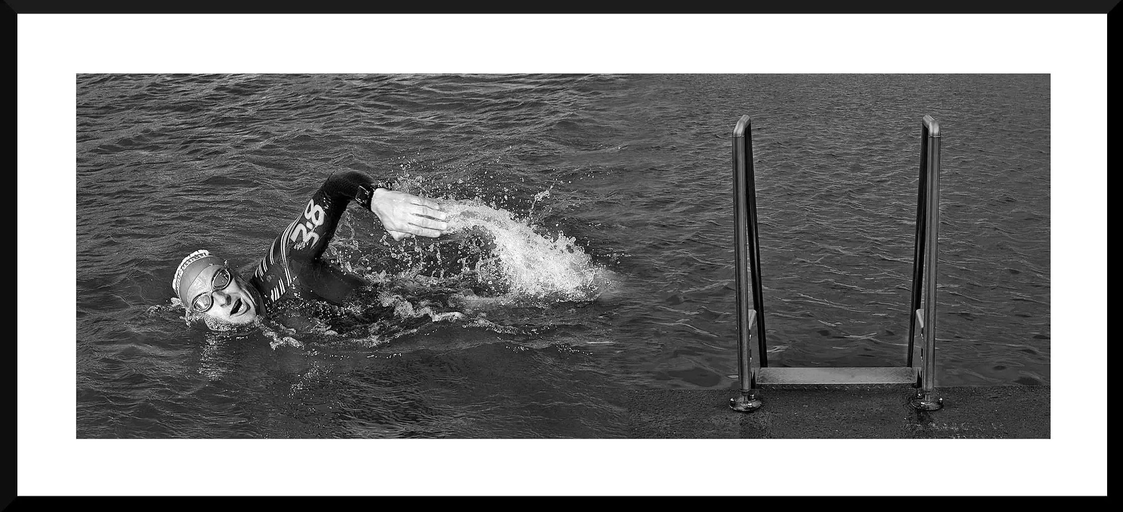 Swimmer in goggles and wetsuit swimming towards a ladder in open water.