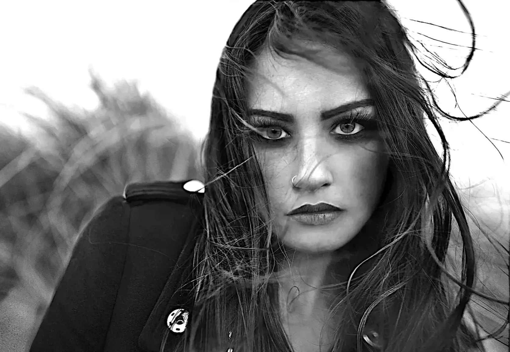 A black and white portrait of a woman with wet hair, intense eyes, and a serious expression, wearing a black jacket with a patch on the shoulder.
