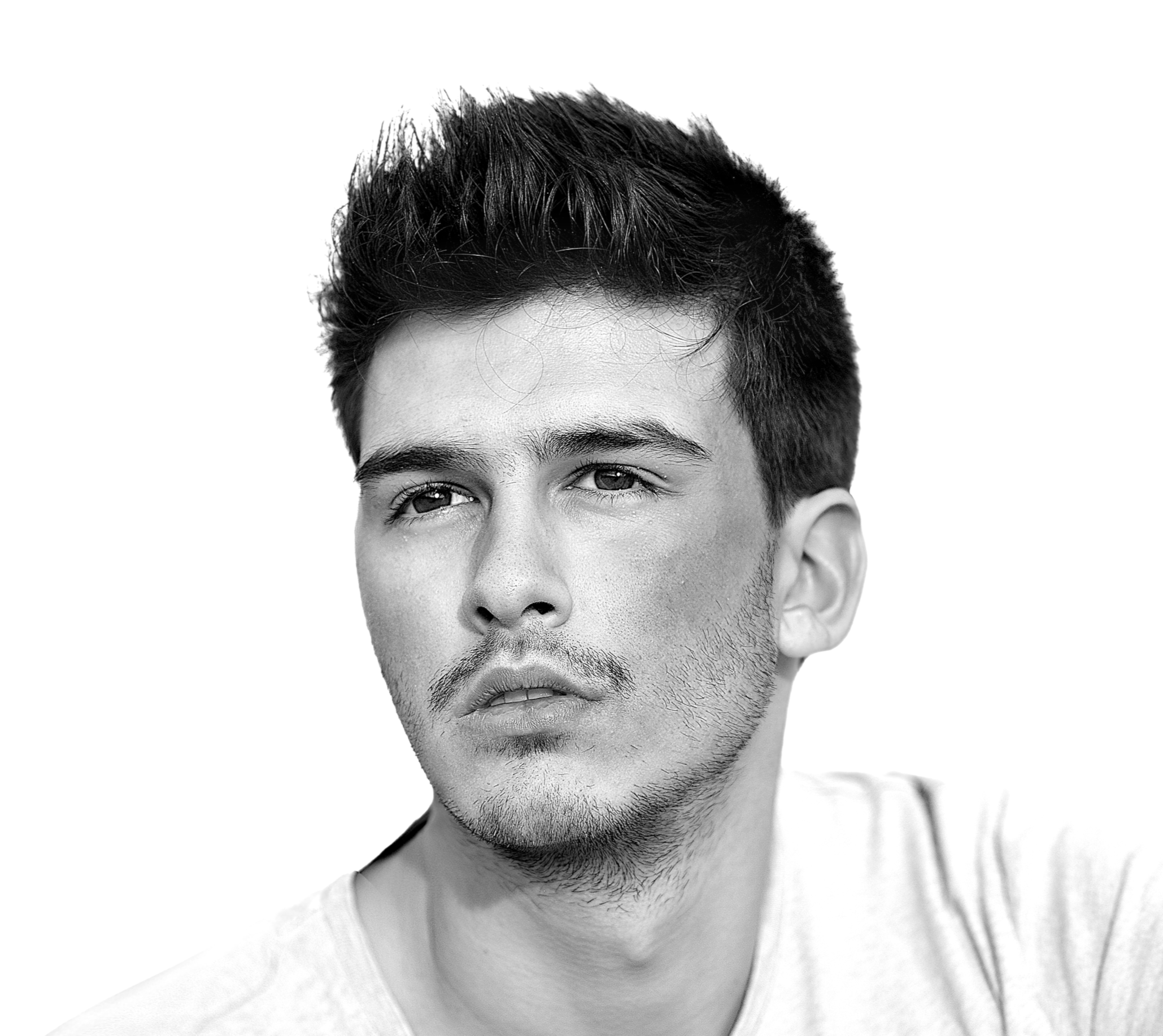 Black and white photograph of a young man with short, styled hair, smiling slightly, wearing a white shirt, with a minimal background.