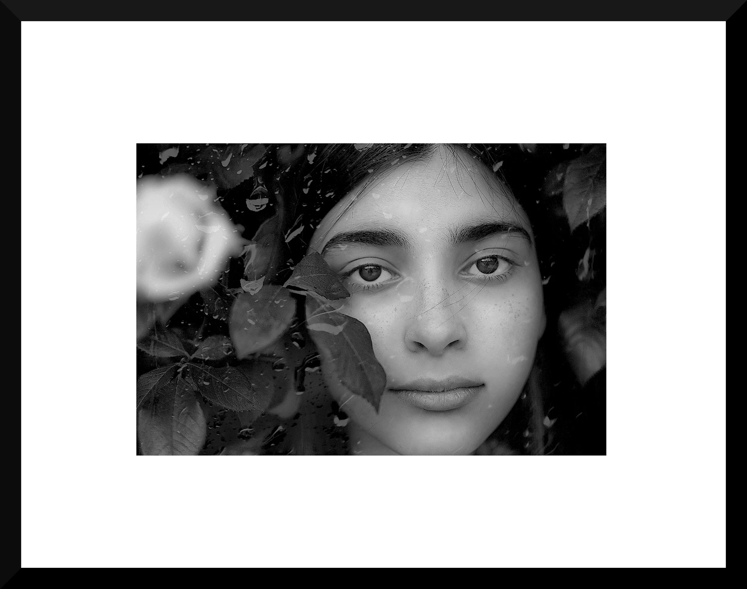 Black-and-white portrait of a young woman with water droplets on her face and leaves around her, looking directly at the camera.