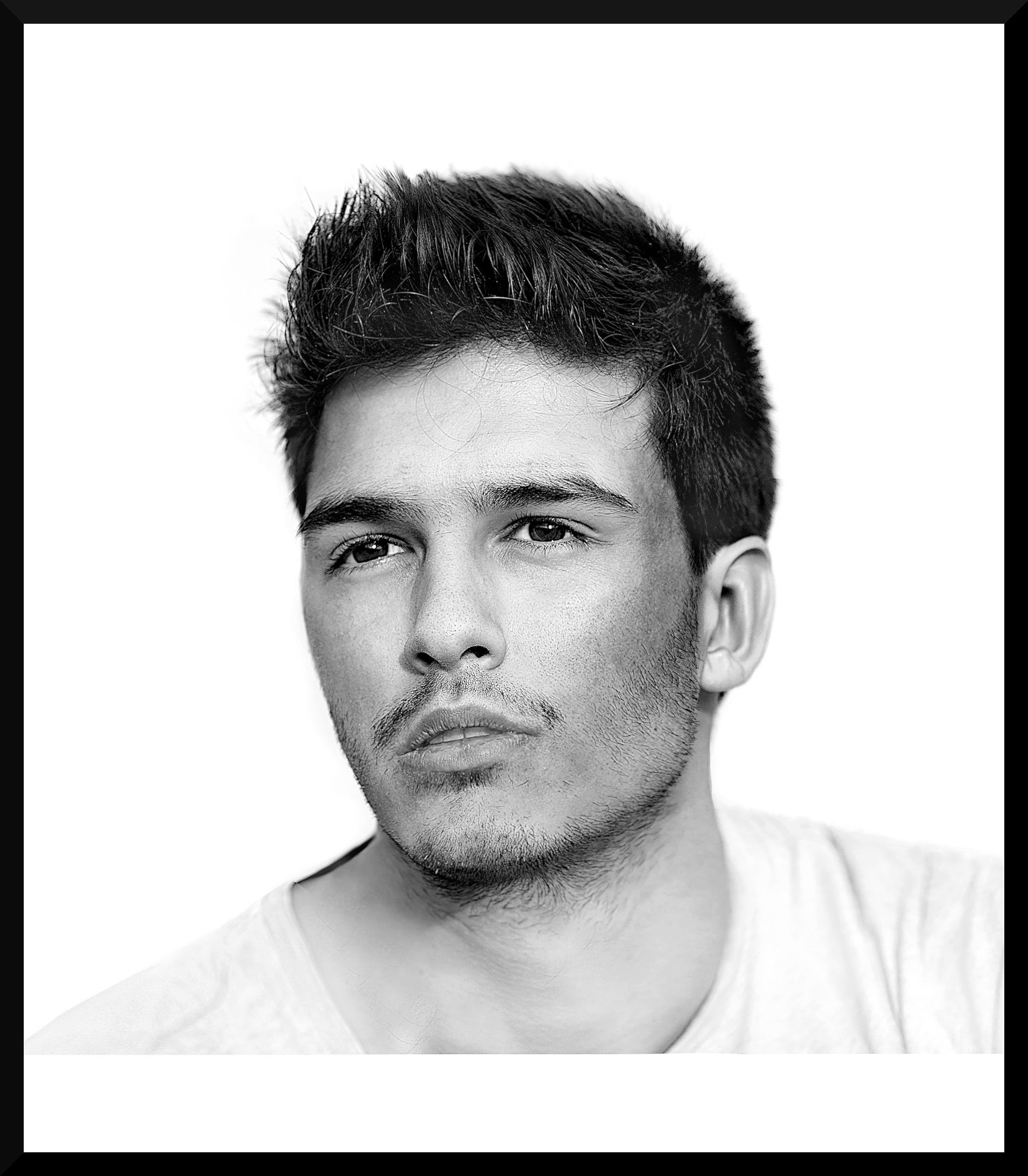 Black and white portrait of a young man with short, slightly messy hair, looking off to the side with a serious expression, wearing a light-colored shirt.