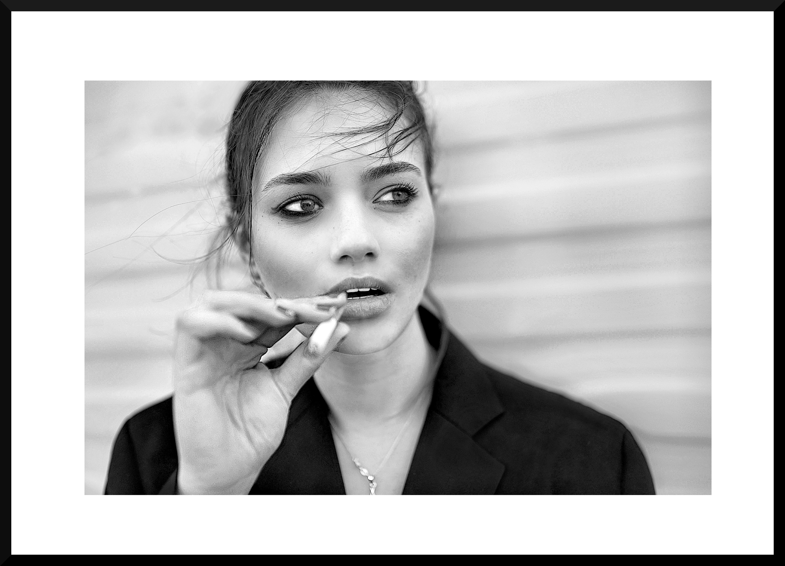 Black and white photo of a woman with short hair holding a cigarette near her lips, looking to the side, standing against a wooden wall.