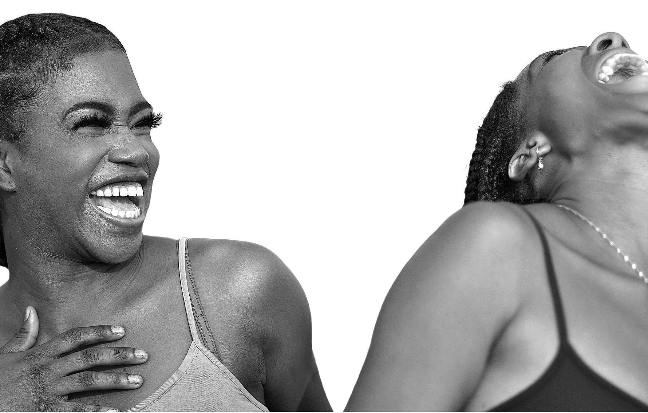 Two women laughing, one with hand on chest and the other with head tilted back, both in tank tops, in a joyful moment.