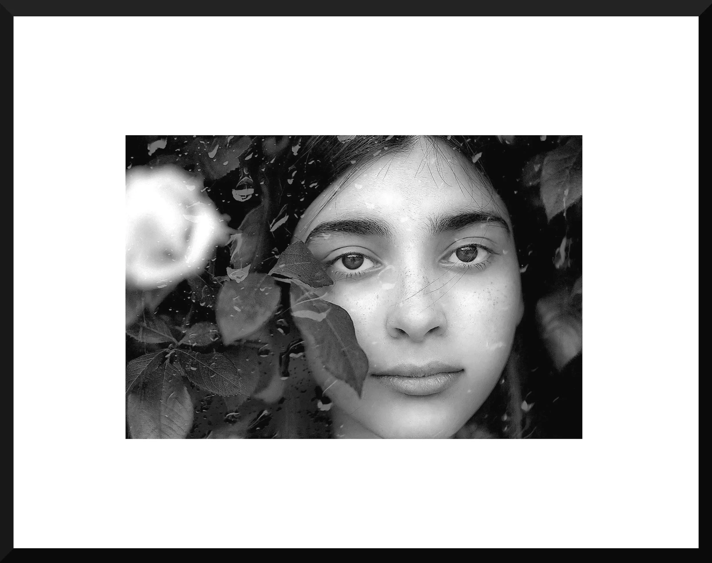 Black and white close-up photo of a girl with water droplets and leaves around her face.