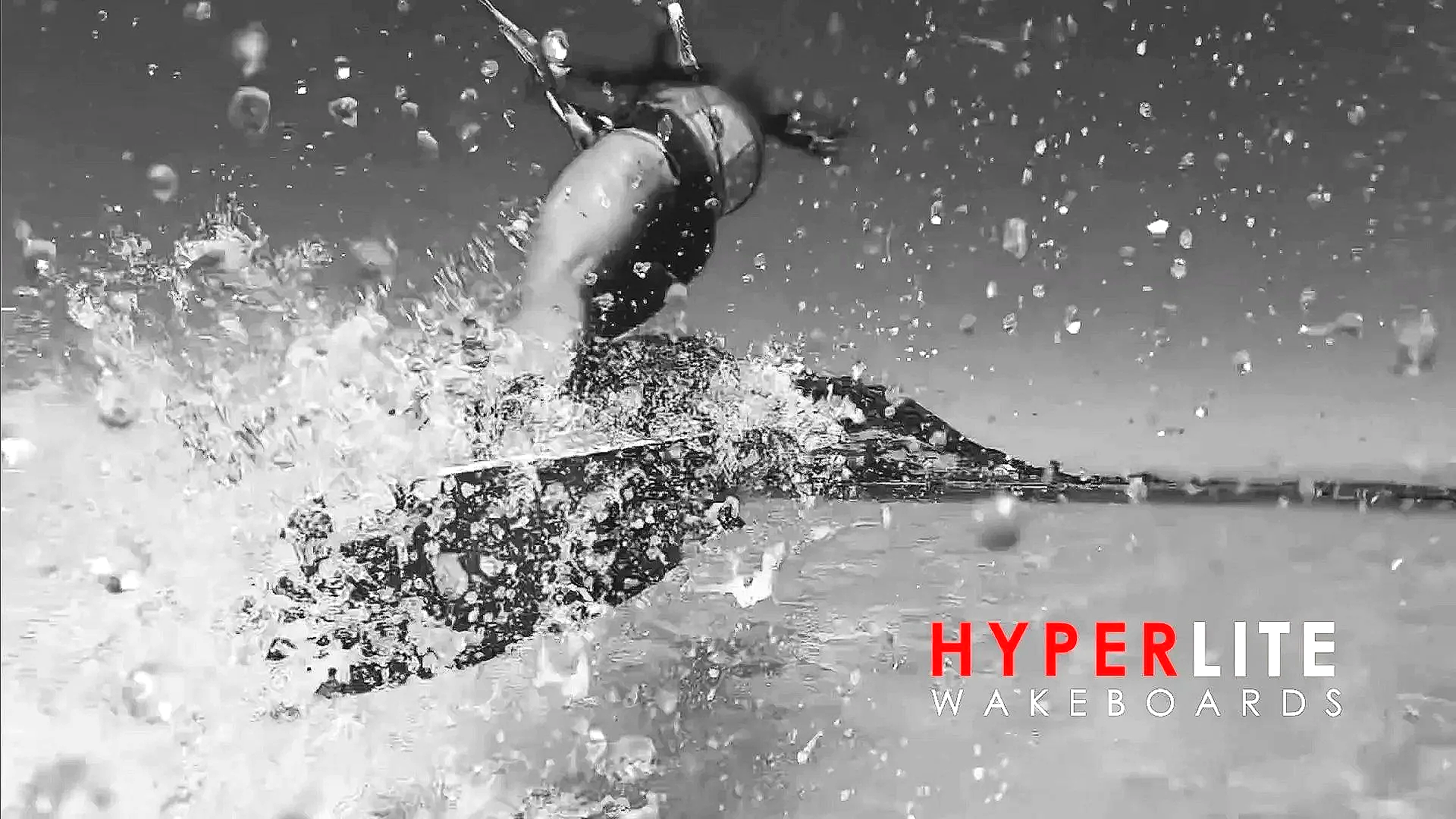 Black and white photo of a wakeboarder performing a jump on the water, creating a splash, with the logo 'Hyperlite Wakeboards' in red and white text at the bottom right corner.