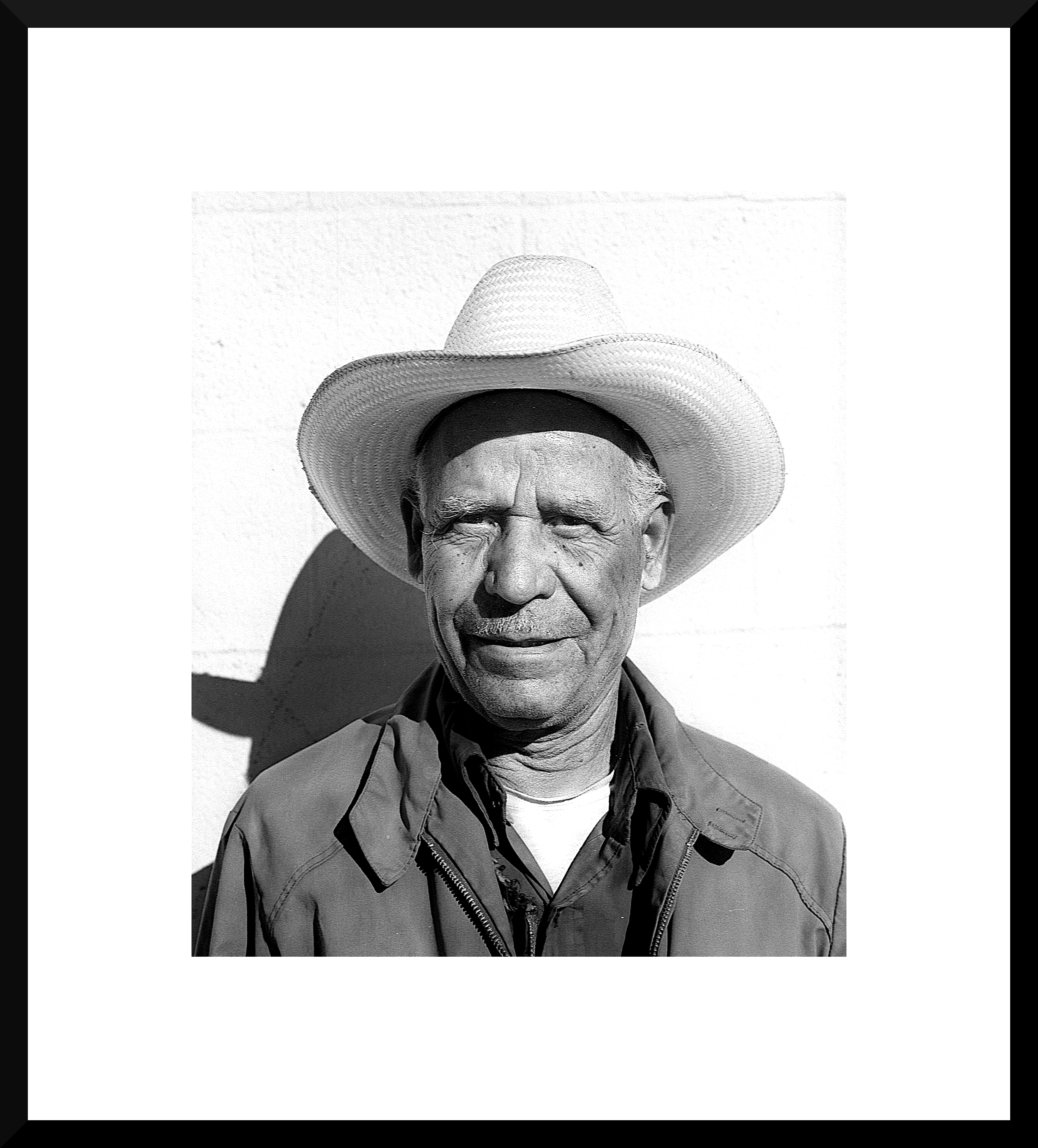 Black and white portrait of an older man wearing a wide-brimmed hat, with a jacket over a shirt, standing against a plain background.