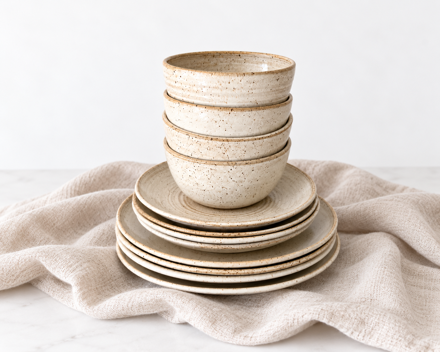 Handmade speckled stoneware dinnerware set featuring stacked ceramic bowls and plates in a warm cream glaze. Service for 4 - breakfast bowl, salad plate and dinner plate.