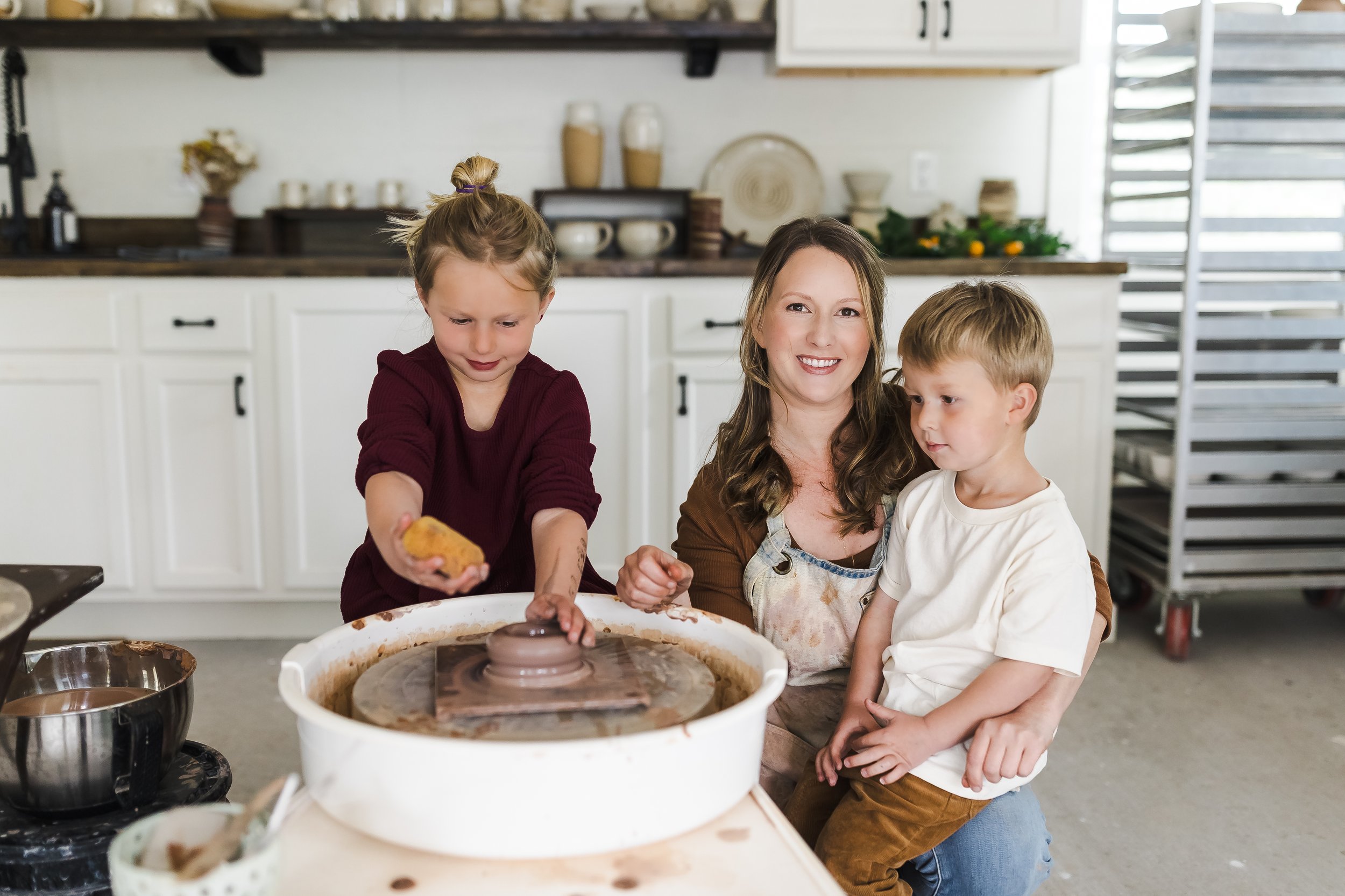 Stephanie Hayes with her children in the Hayes Ceramics pottery studio in Sonoma County, California, gathered around the pottery wheel.