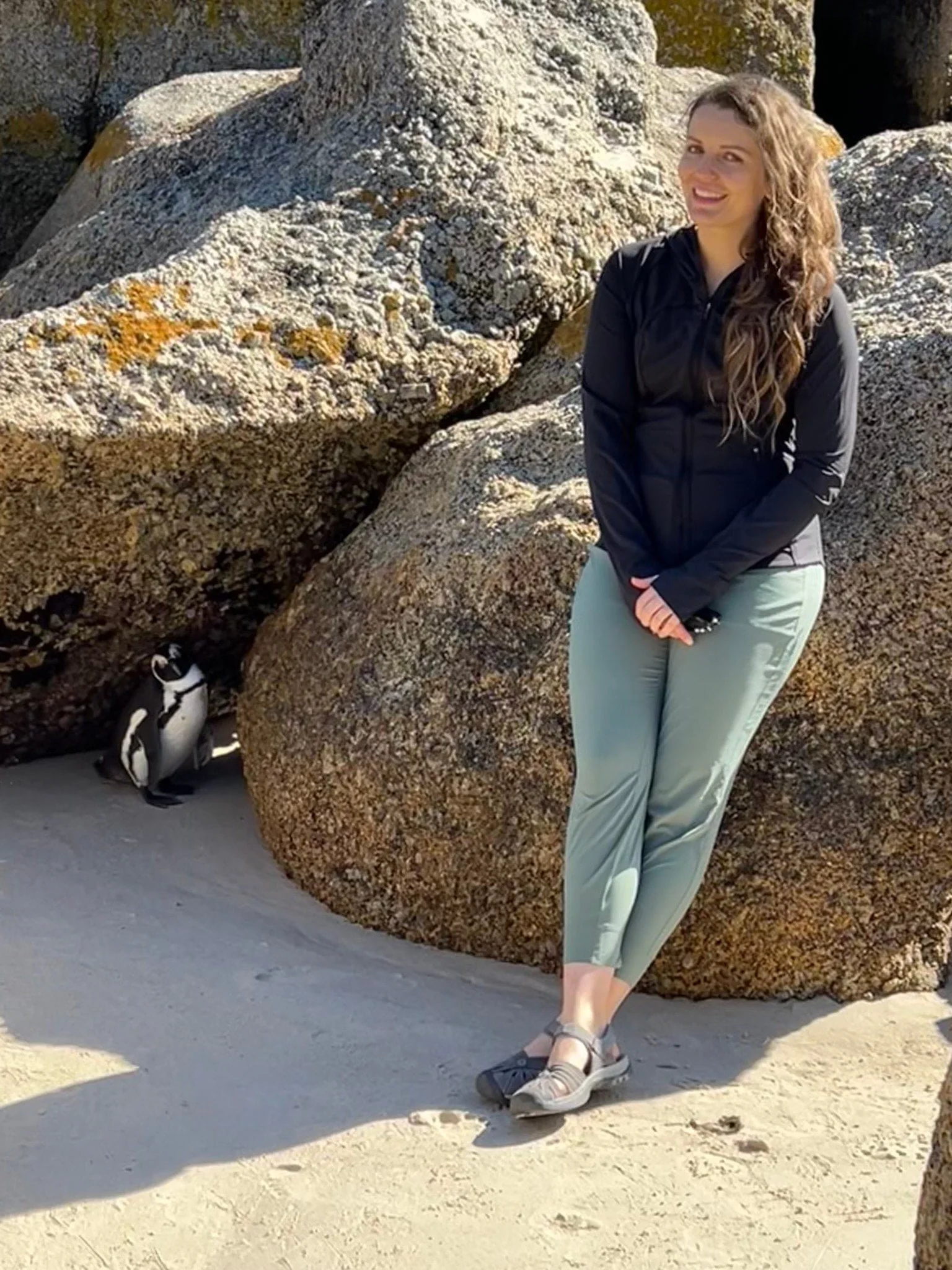 Madeleine standing on beach leaning against a rock