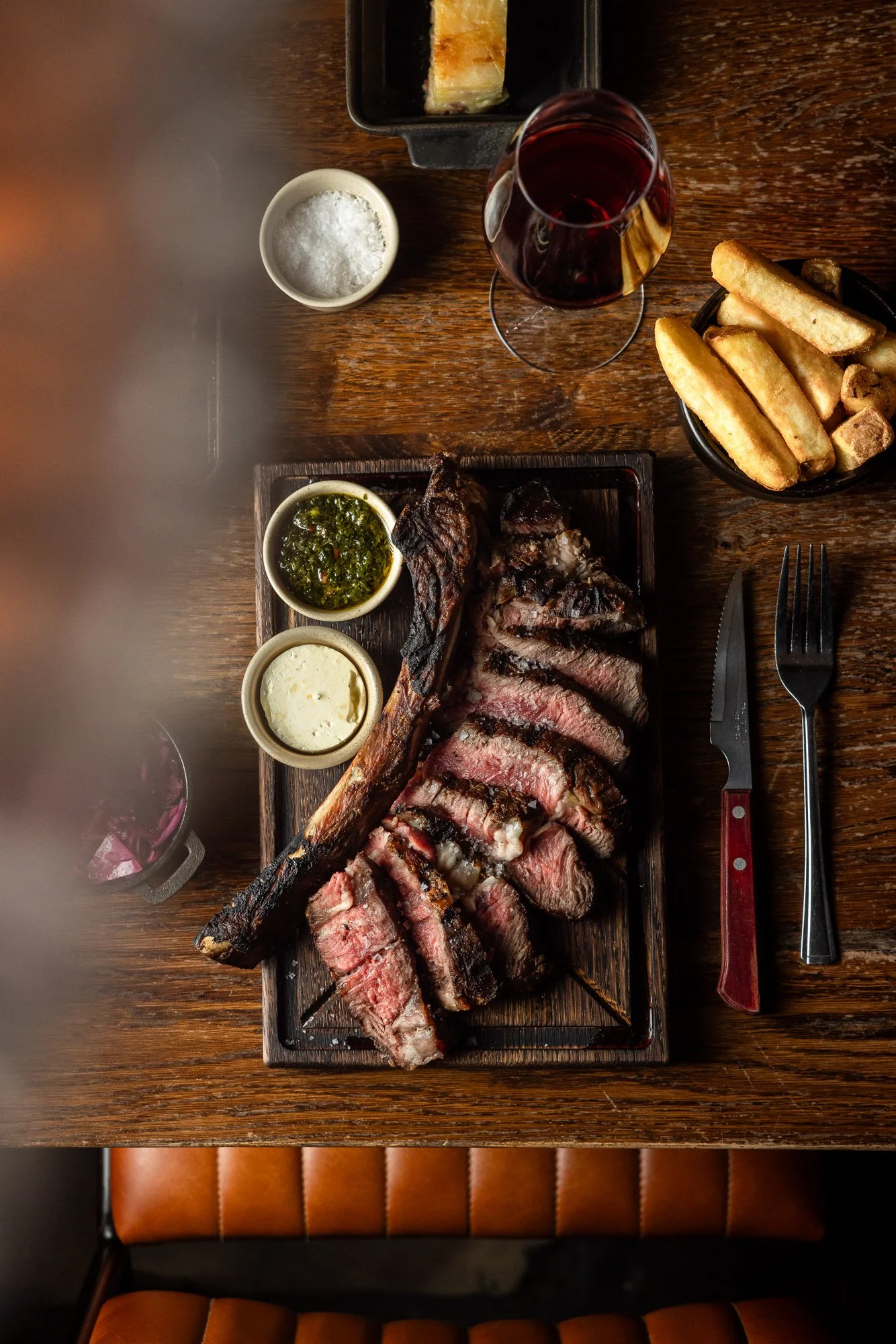 Overhead commercial restaurant photograph of sliced steak served with chips, sauces and red wine at The Cow & Sow in Bristol for menus, websites and hospitality marketing.