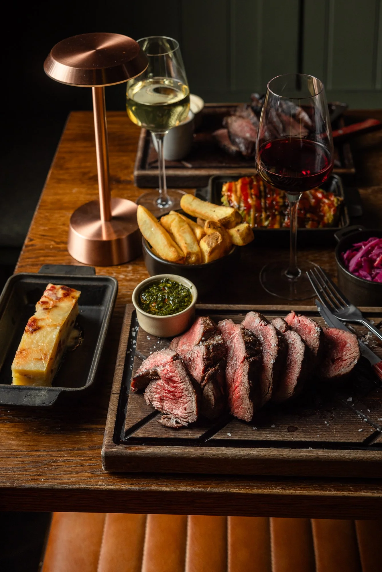 Hospitality food photograph of sliced steak presented with chips, sauces, wine and side dishes across a warmly lit restaurant table, created for Cow and sow steakhouse in Bristol.