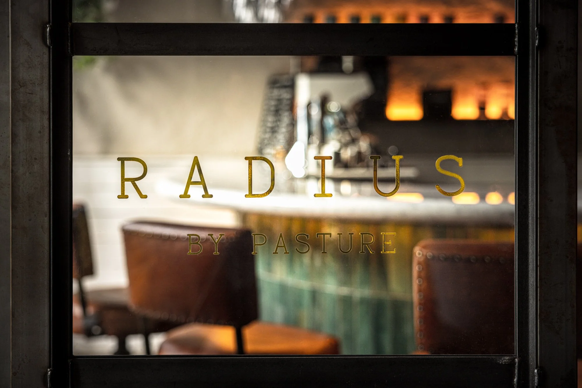 Commercial interior detail of the Radius by Pasture window in Bristol, with leather seating, tiled surfaces and warm restaurant lighting visible through the branded glass.