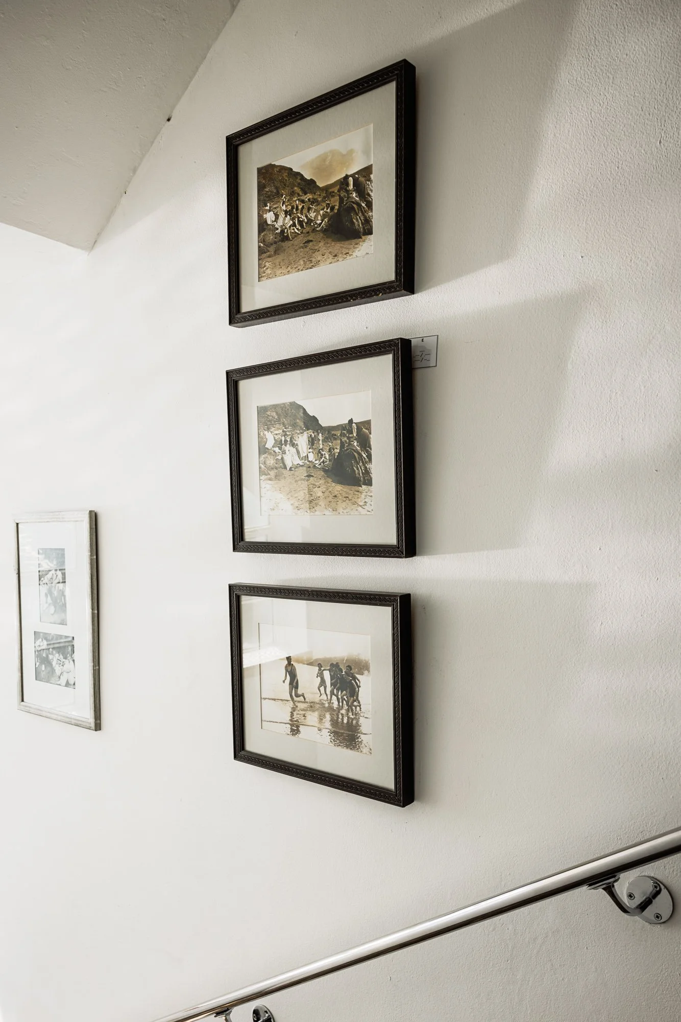 Commercial interior detail at Burgh Island Hotel in Devon, showing framed monochrome artwork arranged along a white stairway wall with restrained spacing and decoration.