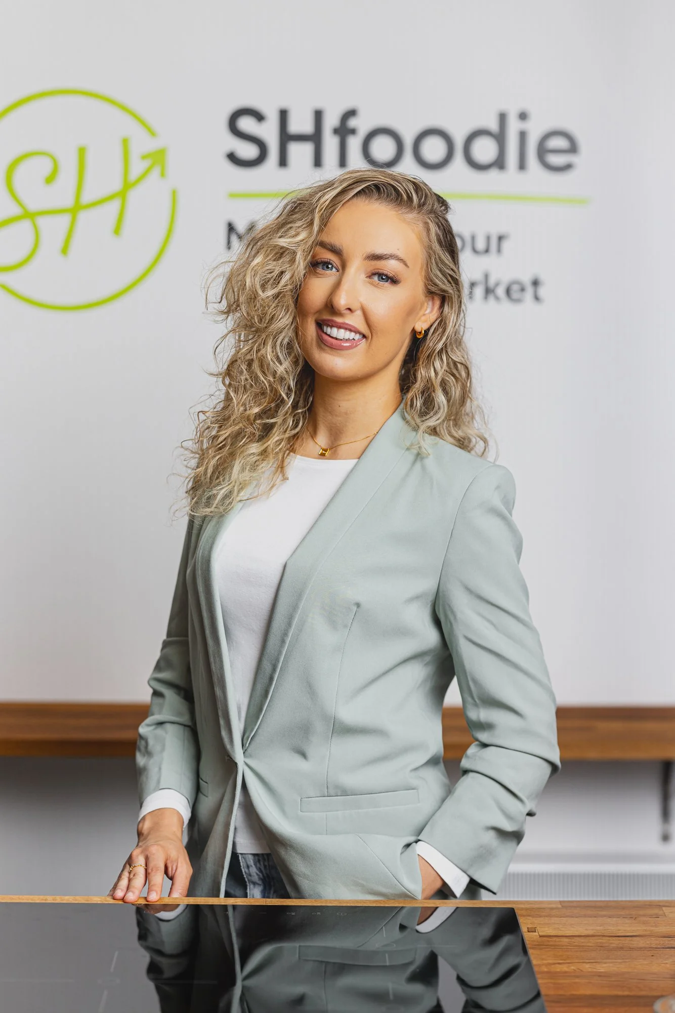 Professional business portrait of a smiling SH foodie representative standing in front of the company branding, using a clear, approachable composition for corporate communication, press, website and professional profile use.