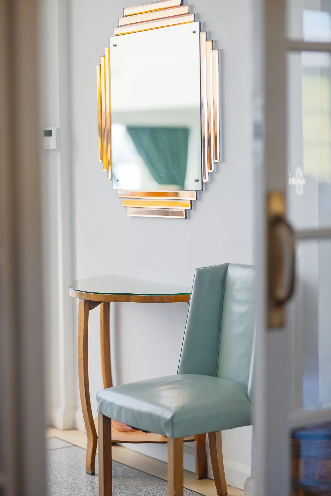 Minimal interior photograph in the Grand Ballroom Restaurant at Burgh Island Hotel in Devon, showing a pale green chair beneath a geometric mirror and small side table.