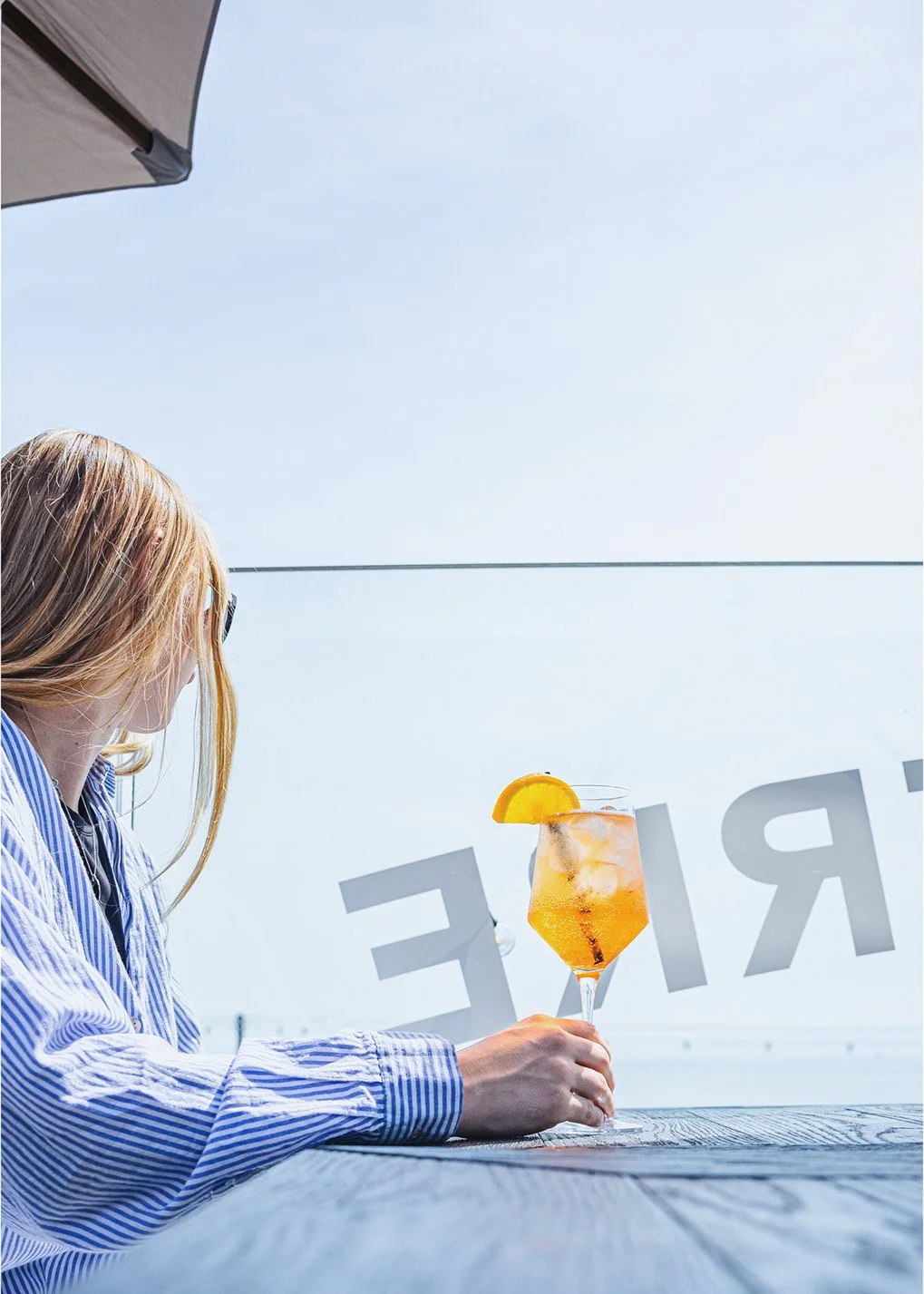 Woman holding an orange cocktail beside the window at Bistrot Pierre in Torquay, photographed for Devon restaurant, drinks, lifestyle and hospitality marketing.