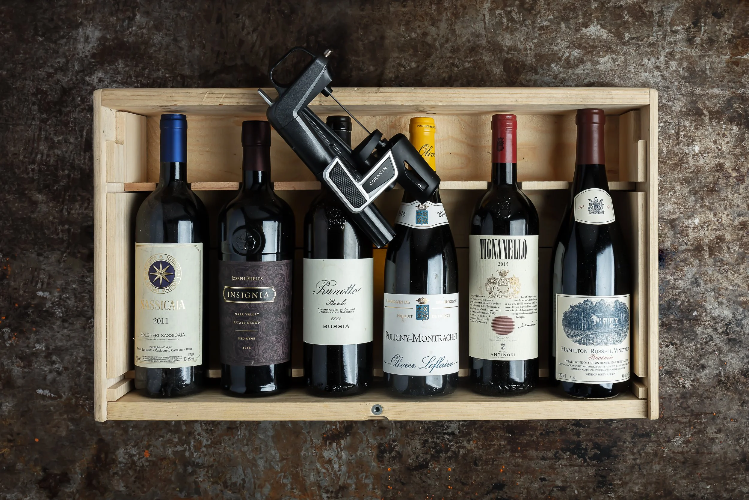 Overhead commercial wine photograph of assorted bottles arranged in an open wooden case with a corkscrew, presenting the range of labels and packaging as a considered product collection for Dine Indulge Bristol.