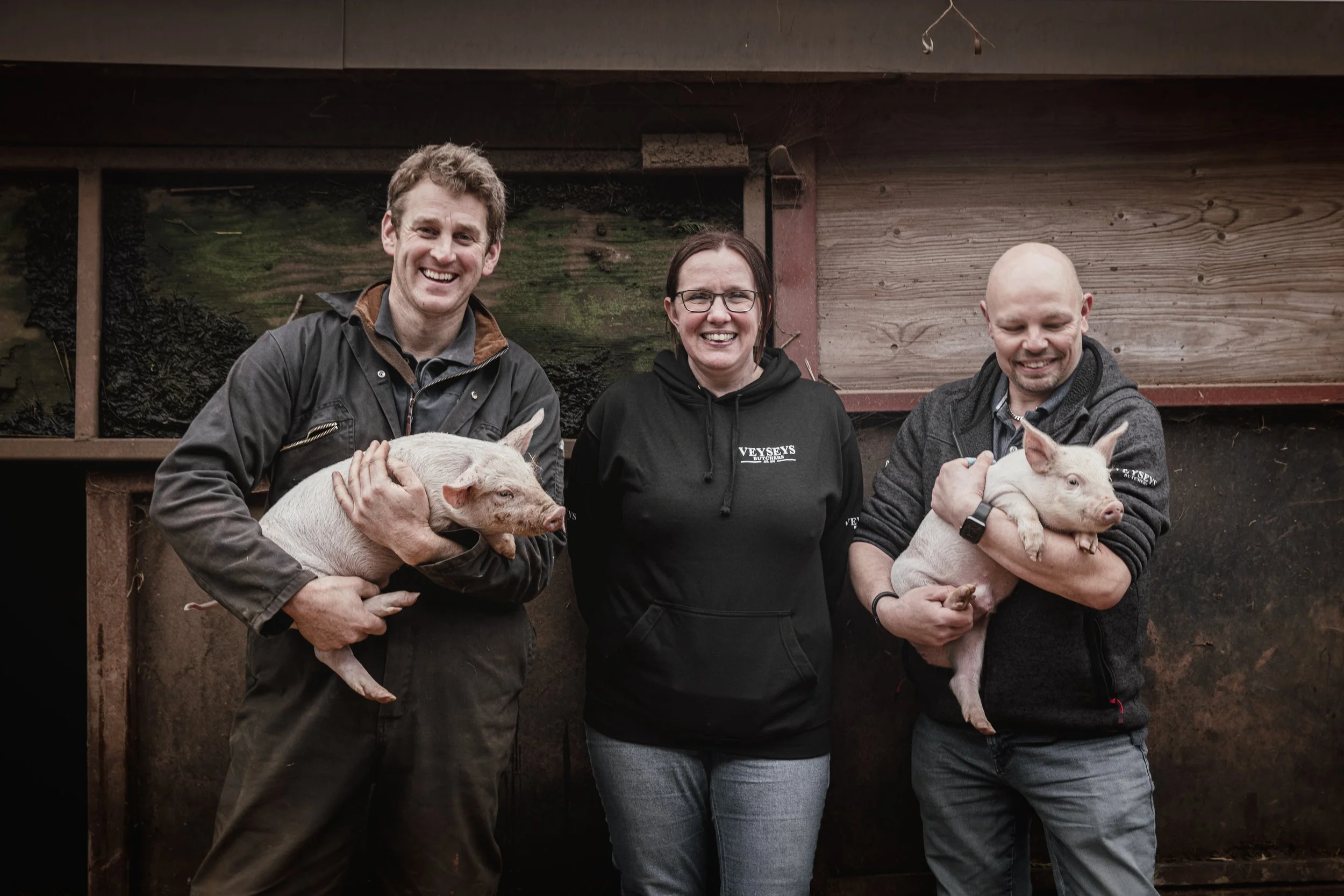 Supplier portrait, three people holding piglets on farm for website bios and press, shot in Stratford-upon-Avon, Warwickshire, partner network in Poole, Dorset, for use in London and Truro, Cornwall.