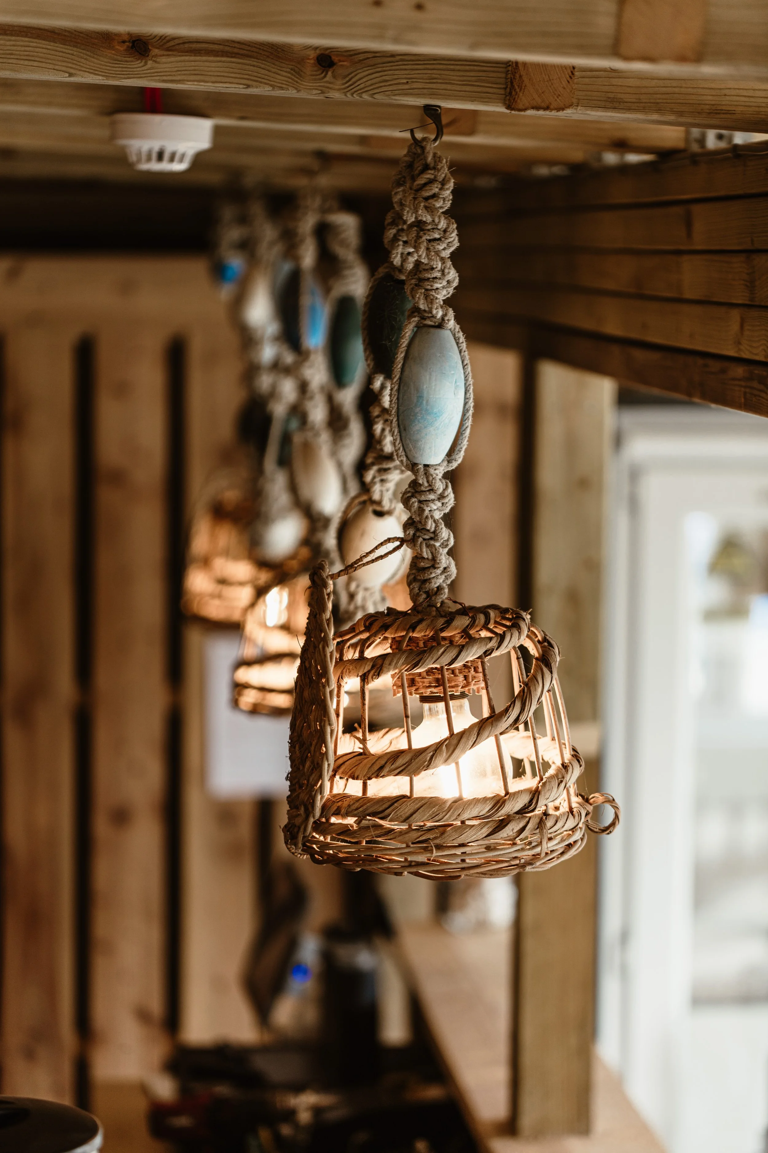 Close interior photograph of a woven pendant light at Lula Shack in Cornwall, suspended from thick rope and framed by warm timber to emphasise its handmade texture.