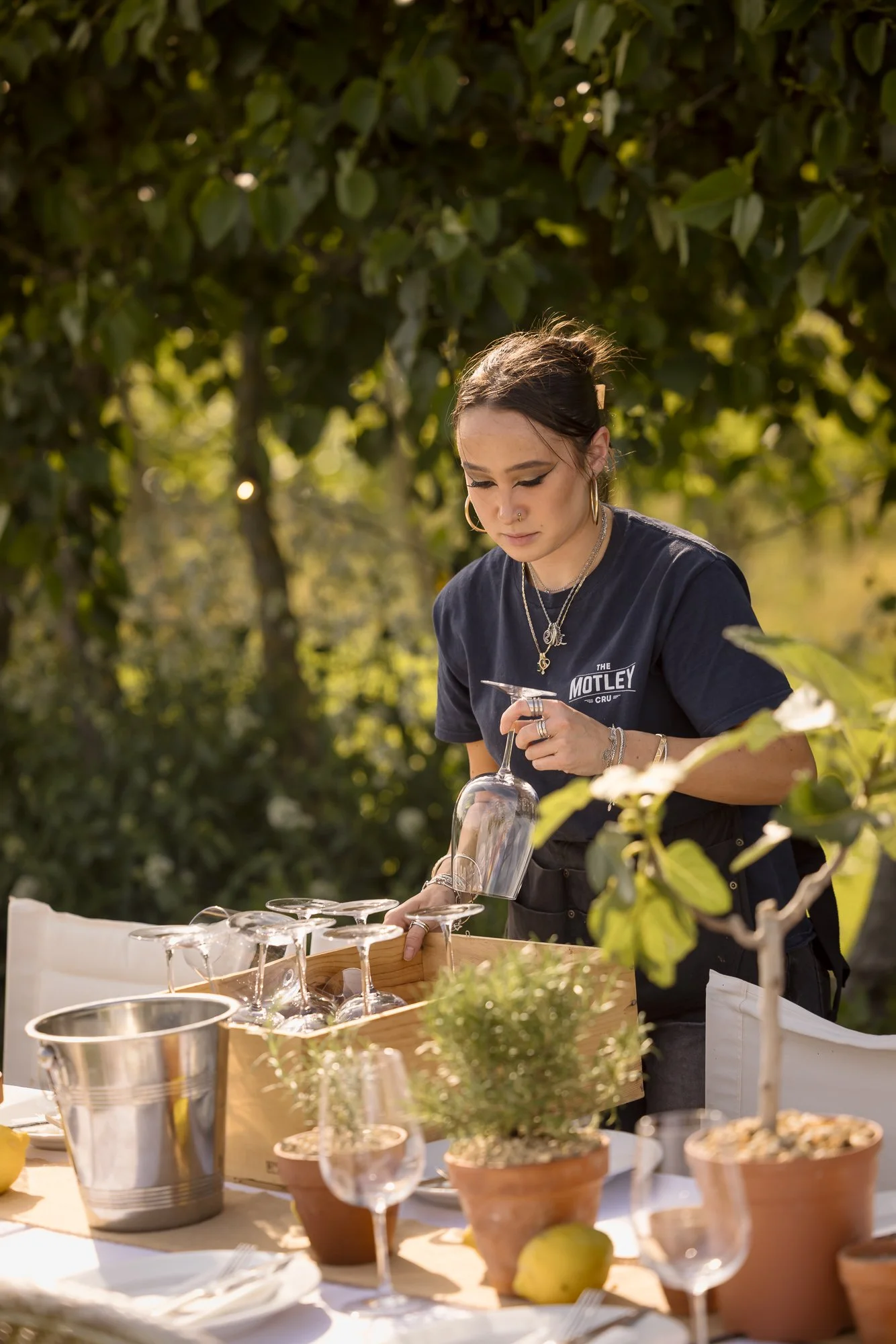Candid hospitality photograph of a team member preparing glasses and tableware during outdoor service, using the vineyard setting and natural working gesture to show the practical preparation behind Kenton Park Estate in Exeter, Devon.