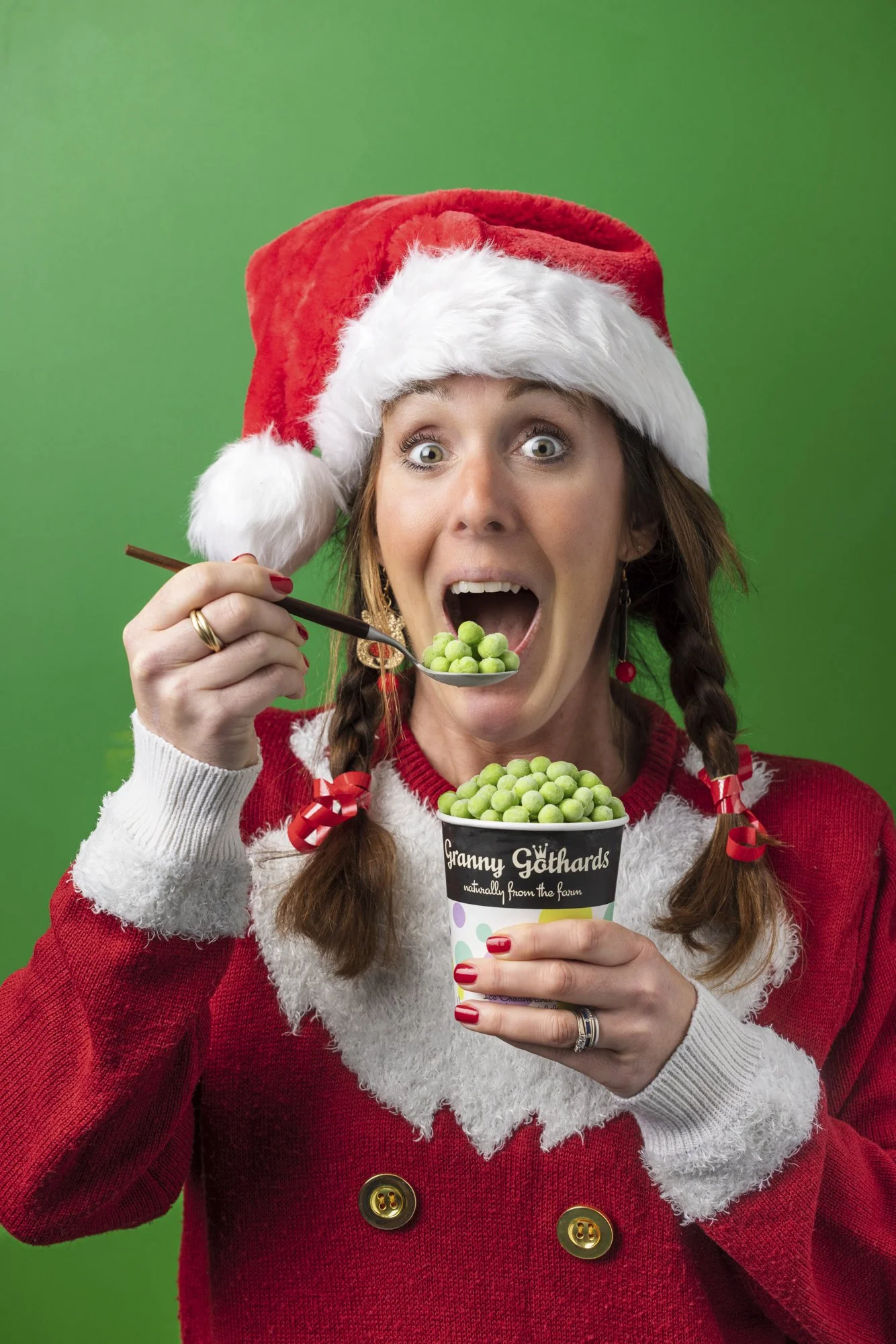 Colourful seasonal portrait of a woman in a Santa costume reacting playfully while eating green ice-cream from a branded tub, photographed against a vivid green background for Granny Gothards in Devon.