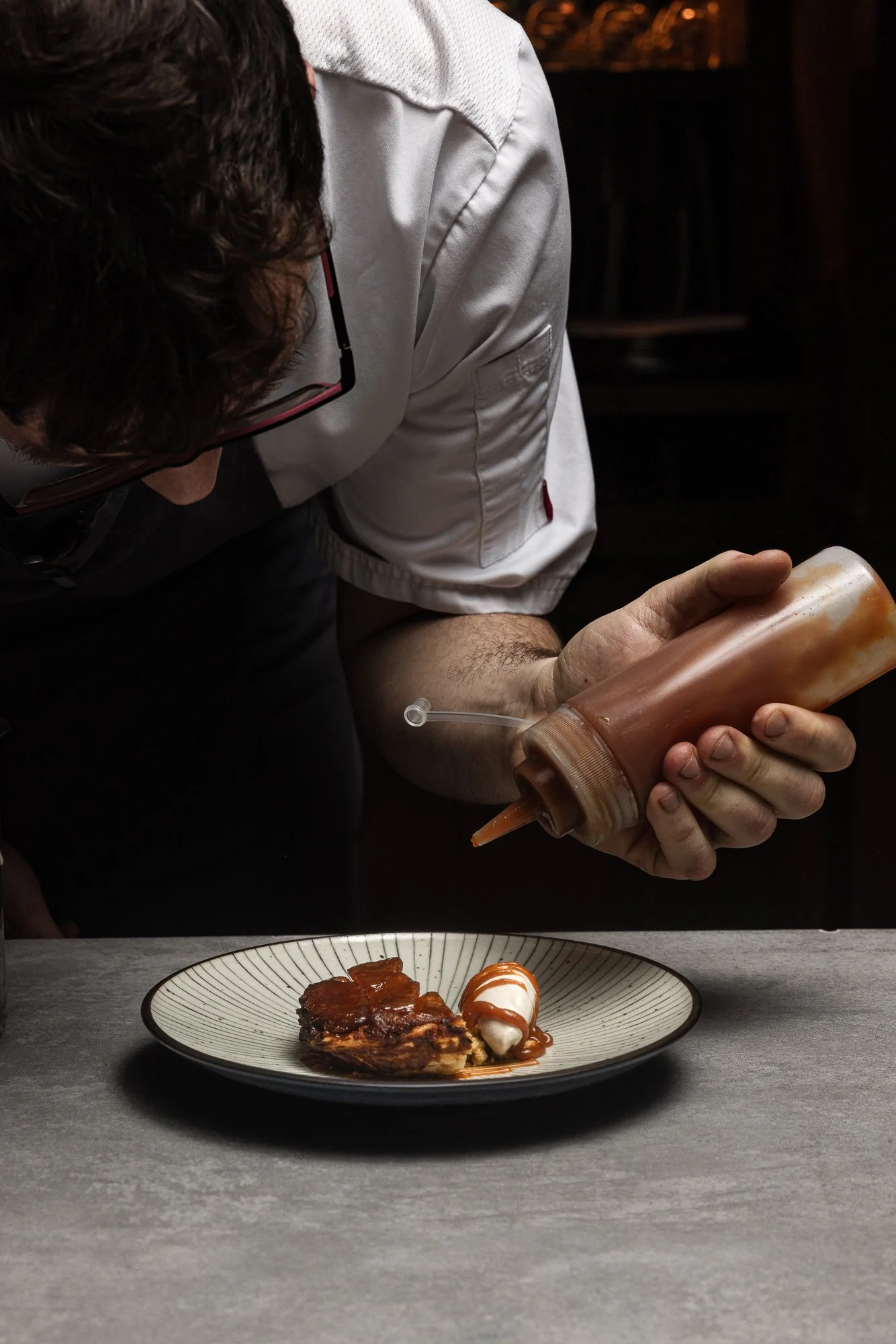 Kitchen action, chef saucing a plated dessert at the pass for PR and editorial, shot in Cirencester, Gloucestershire, venue marketing in Marlborough, Wiltshire, for use in London and the Cotswolds.
