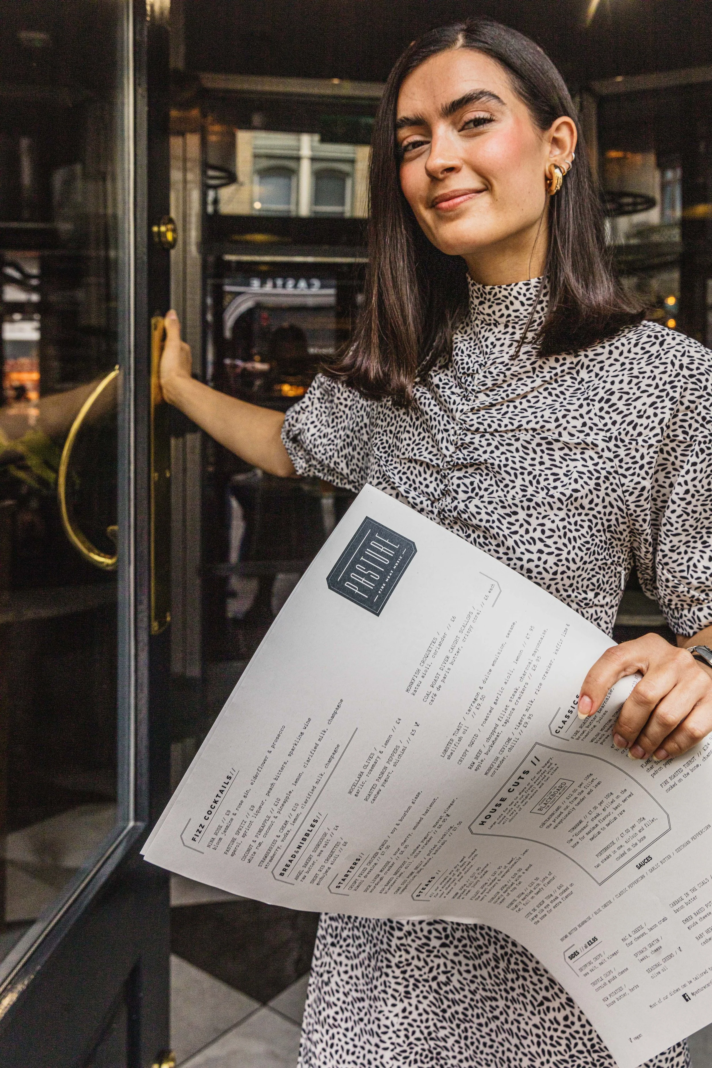 Environmental portrait of a restaurant hostess standing at the entrance with a printed menu in hand, photographed in the working venue to show the person and guest-facing role for The Mole Resort in Devon.