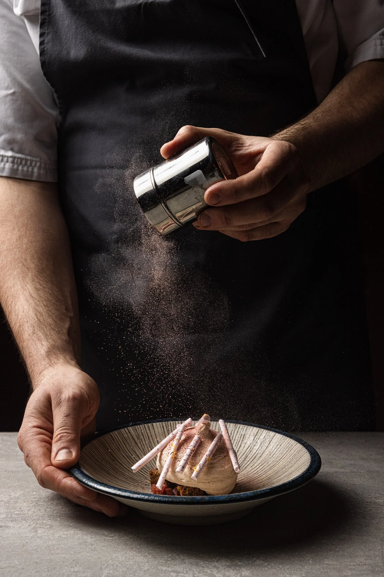 Kitchen action, chef dusting dessert with a fine shaker for menus and social, shot in Bristol, Somerset, venue marketing in Plymouth, Devon, for use in London and Oxford, Oxfordshire.