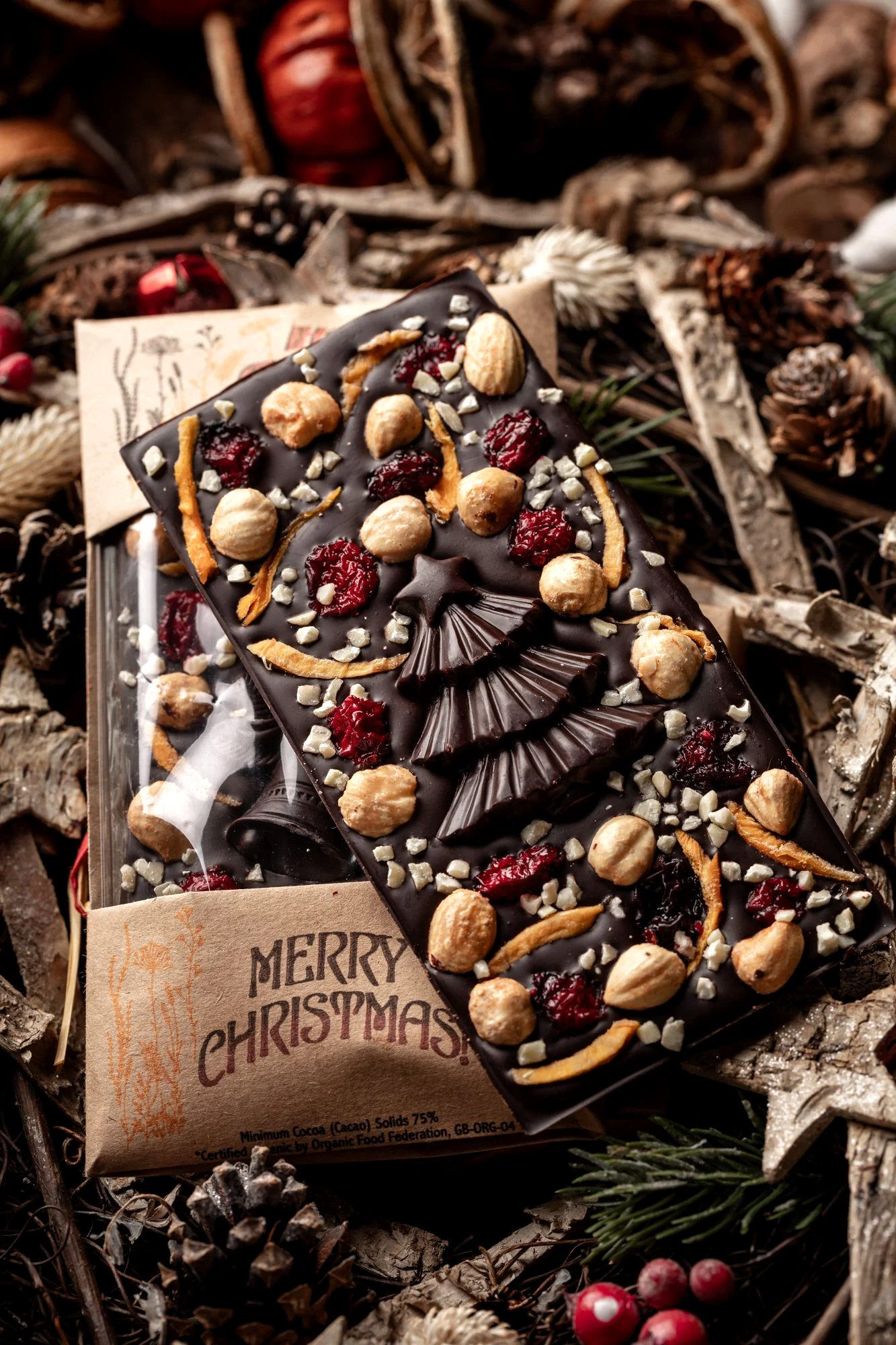Seasonal commercial photograph of a decorated chocolate slab covered with nuts, dried fruit and festive toppings, presented in textured Christmas packaging for Honey Chocolate seasonal campaign in Devon.