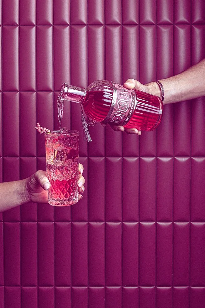 Pink spirit poured from a Coastal Distilling Co bottle into a glass against a matching pink interior, photographed in Devon for drinks, cocktail and product marketing.