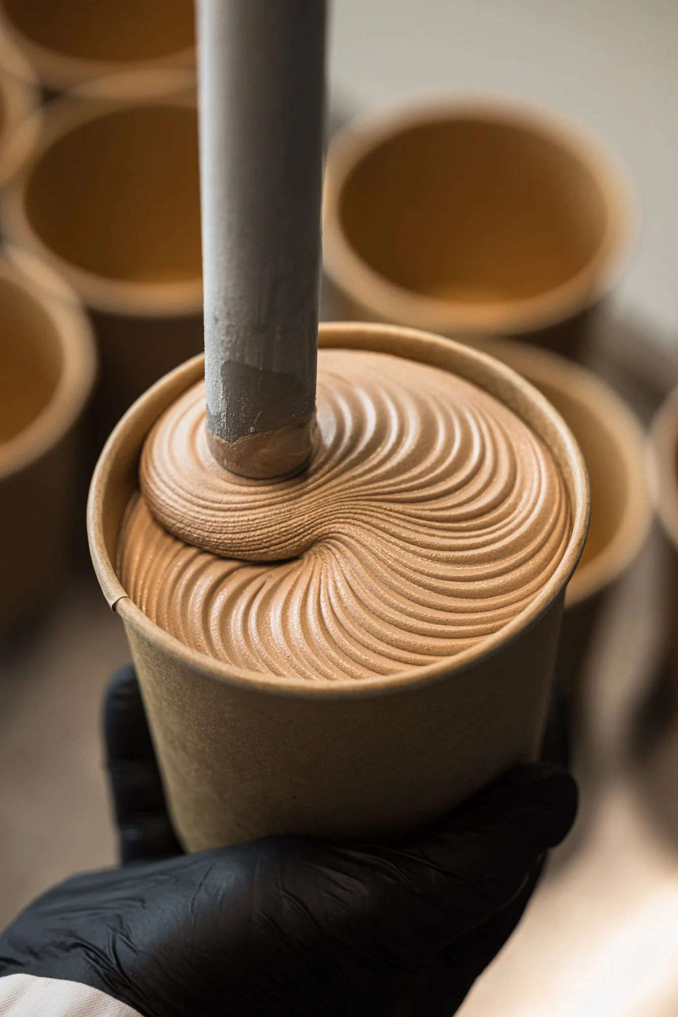 Commercial production photograph of smooth chocolate-coloured gelato being dispensed into a paper container, capturing its spiral texture and the controlled filling process for Granny Gothards in Devon
