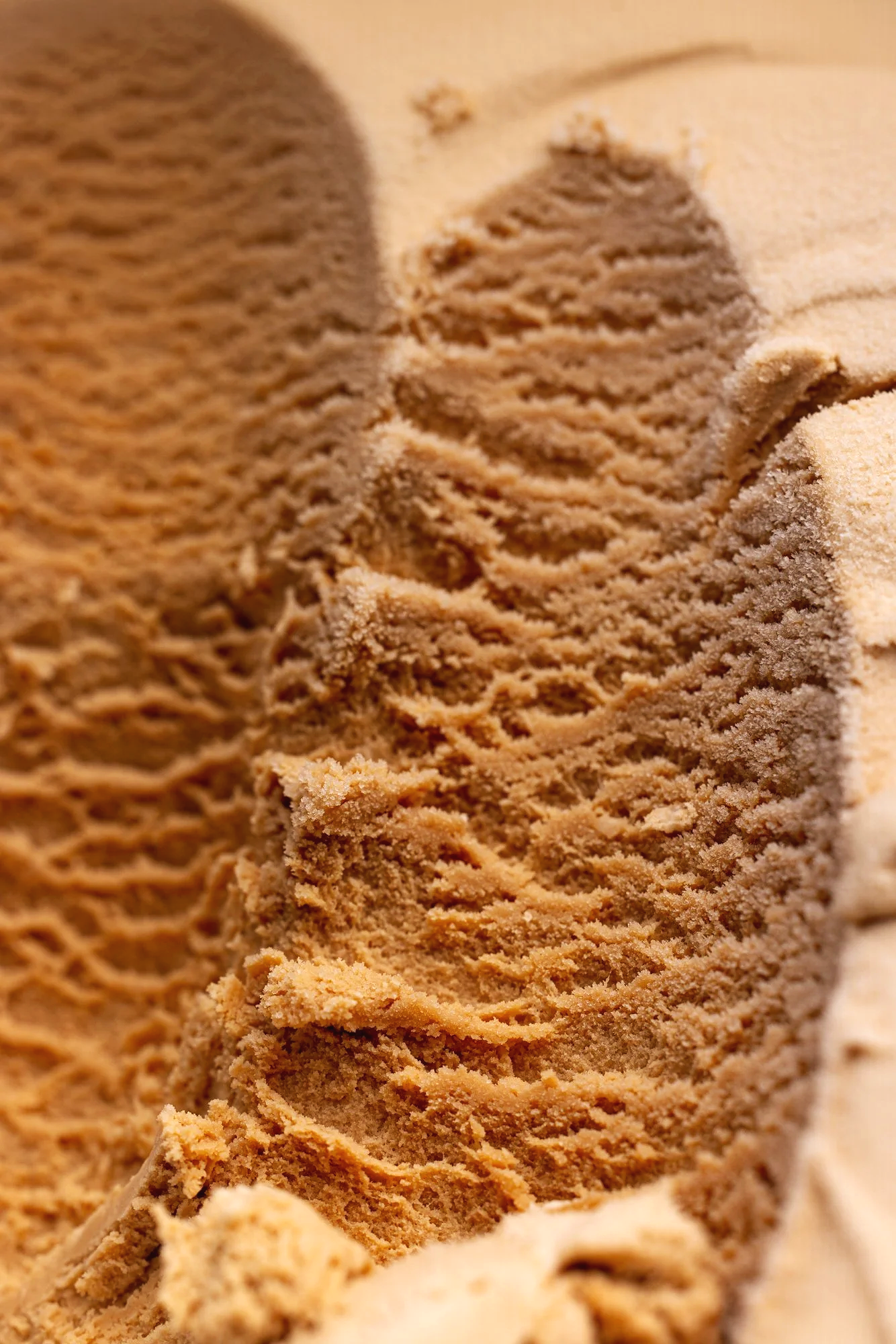 Macro commercial photograph of freshly worked brown ice-cream or gelato, revealing ridges, scooped texture and fine surface detail for ice-cream producer, brand or editorial project.