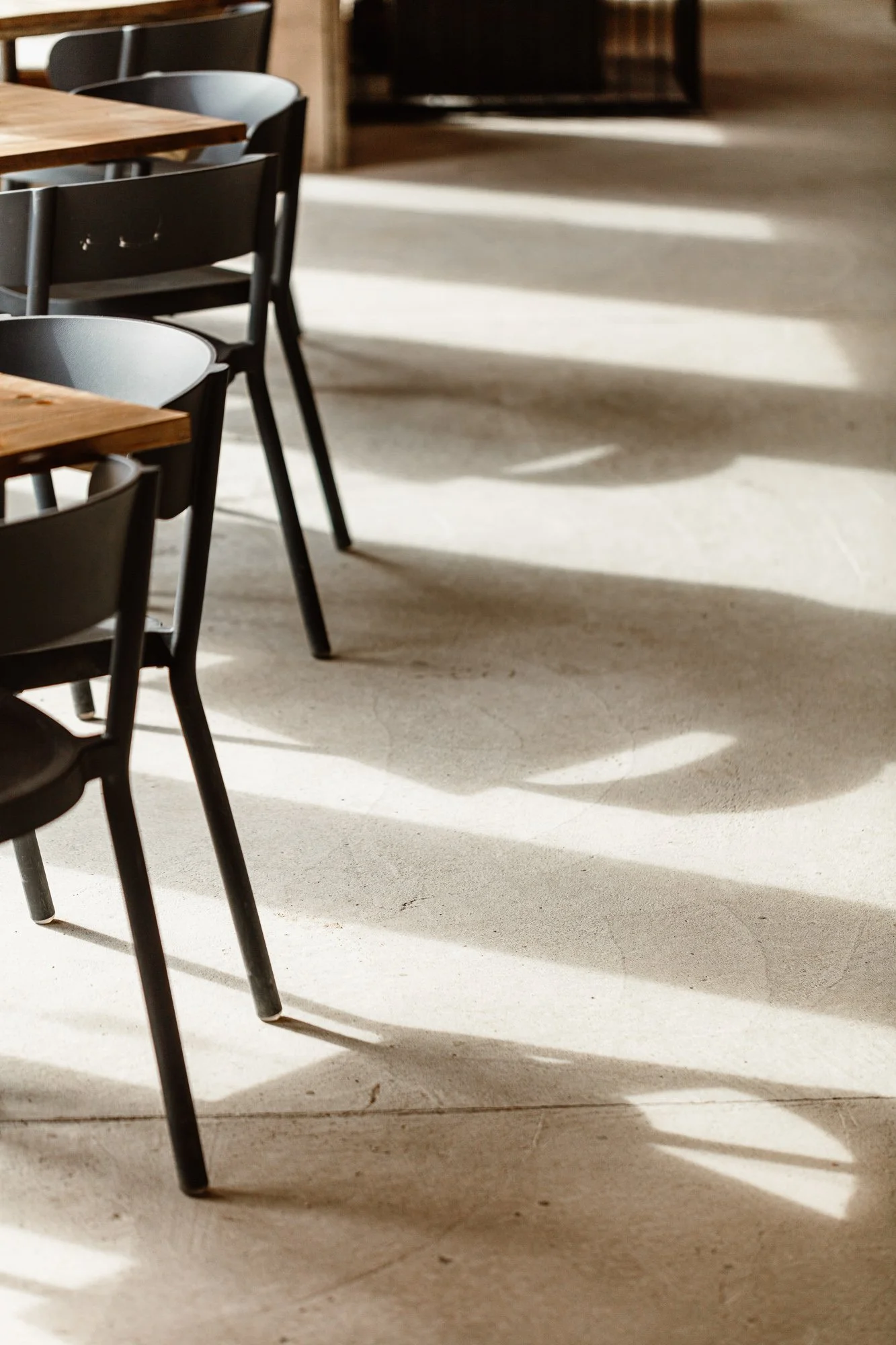 Graphic interior detail at Lula Shack in Cornwall, showing black dining-chair legs and strong window shadows crossing the pale stone floor in repeated lines and shapes.