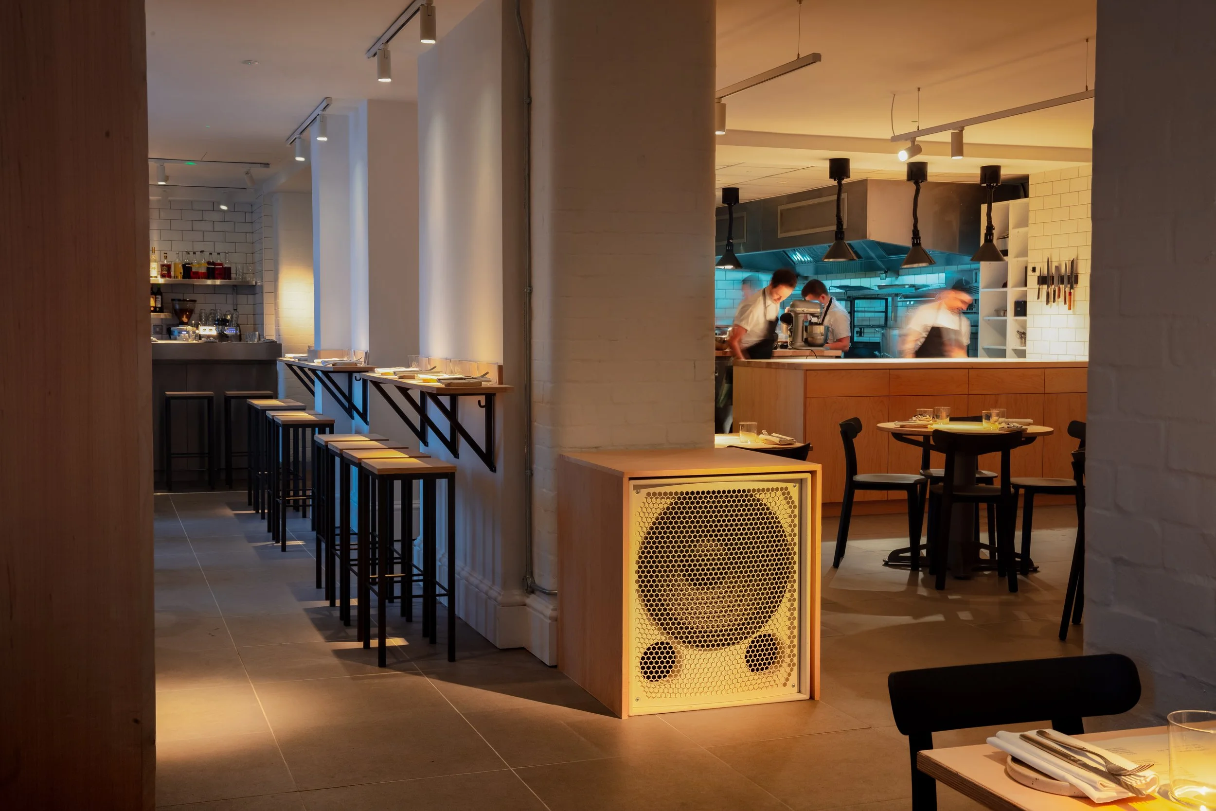 Commercial interior photograph of Casamia by Peter Sanchez-Iglesias in Bristol, showing white columns, counter seating, laid tables and chefs working in the open kitchen.