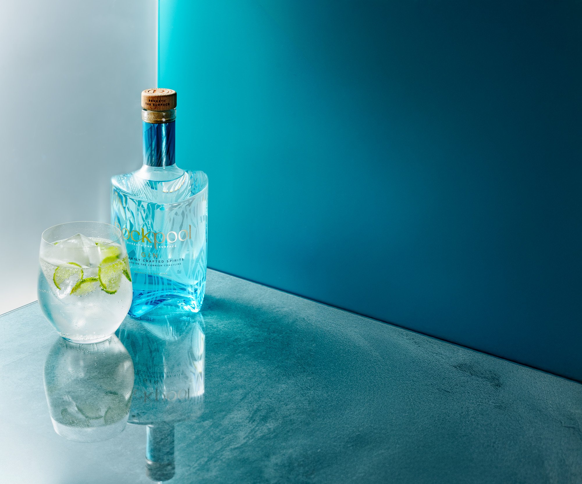 A gin and elderflower tonic served in a coupe glass, alongside a detailed gin bottle, photographed in a stylish bar in Plymouth, Devon, using botanicals sourced from Torquay, Devon, for hospitality promotions in Newquay, Cornwall, and London.