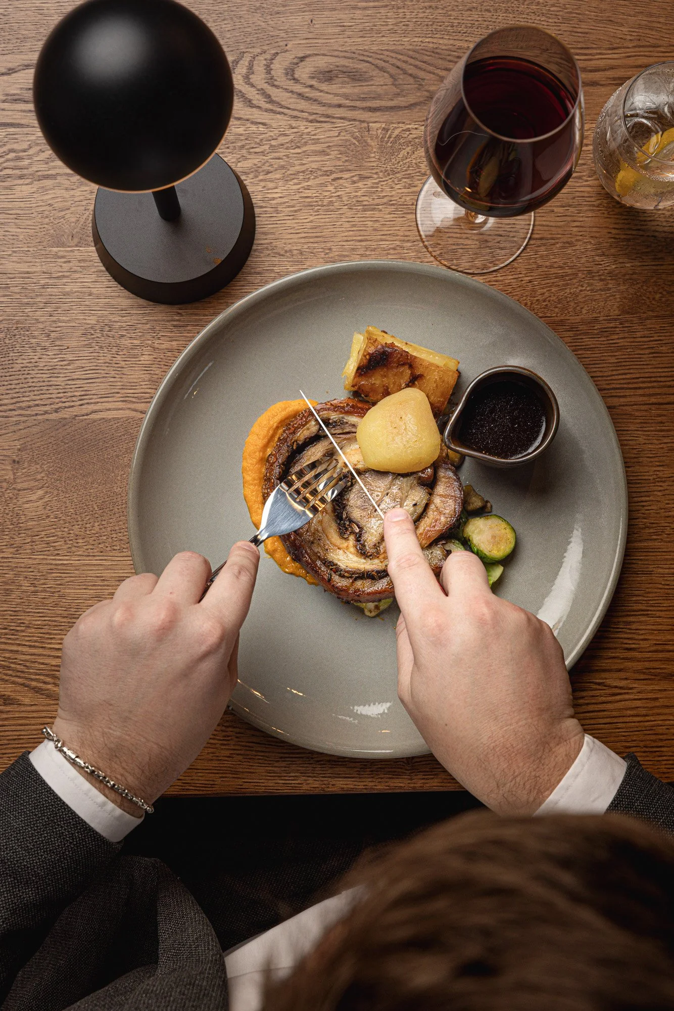 Overhead restaurant photograph showing a diner cutting into roast dinner at a set table with wine, crockery and serving details, capturing the meal in context for Chef Culture in Bristol