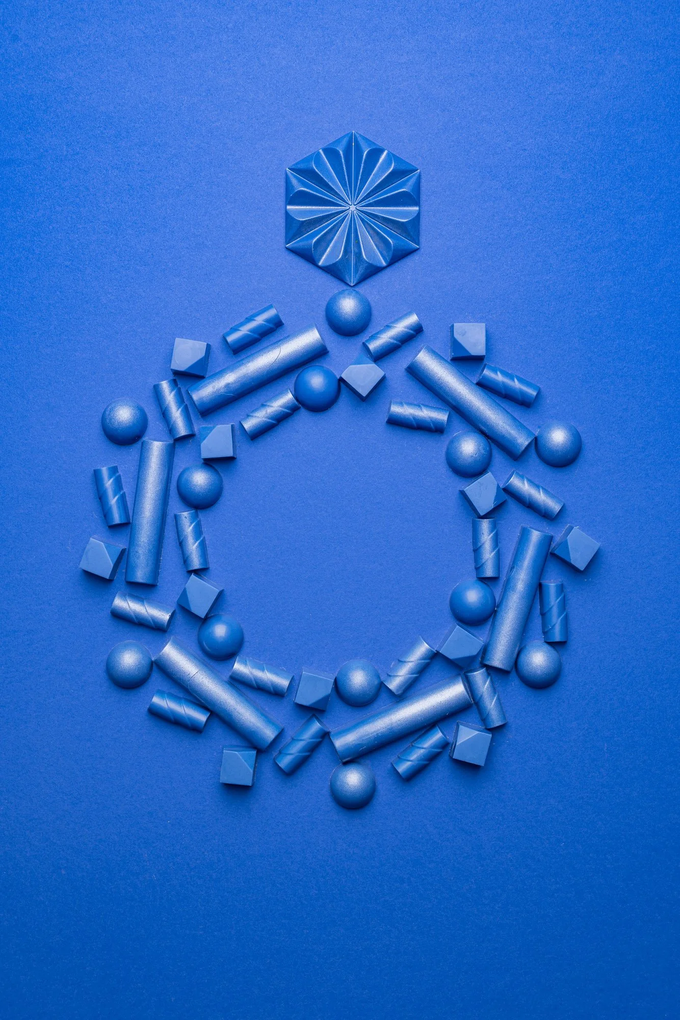 Graphic commercial photograph of blue chocolate pieces and moulded shapes arranged into a circular design on a matching blue background, created as a precise product-led composition for DeZaan Christmas communication.