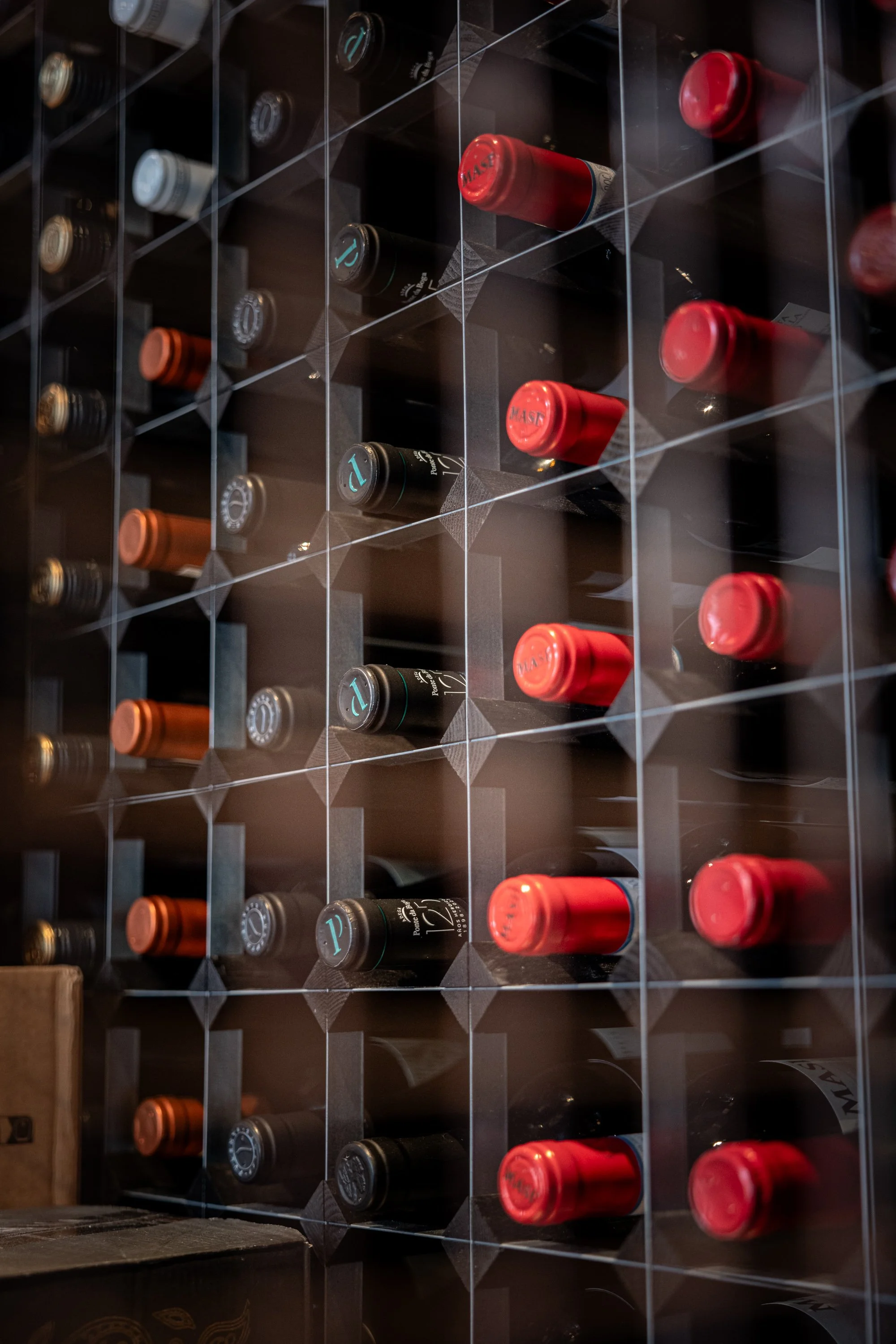 Close commercial interior photograph at The Nest Restaurant, The Feathers Hotel, showing wine bottles stored in a geometric rack with repeating red capsules and dark glass.