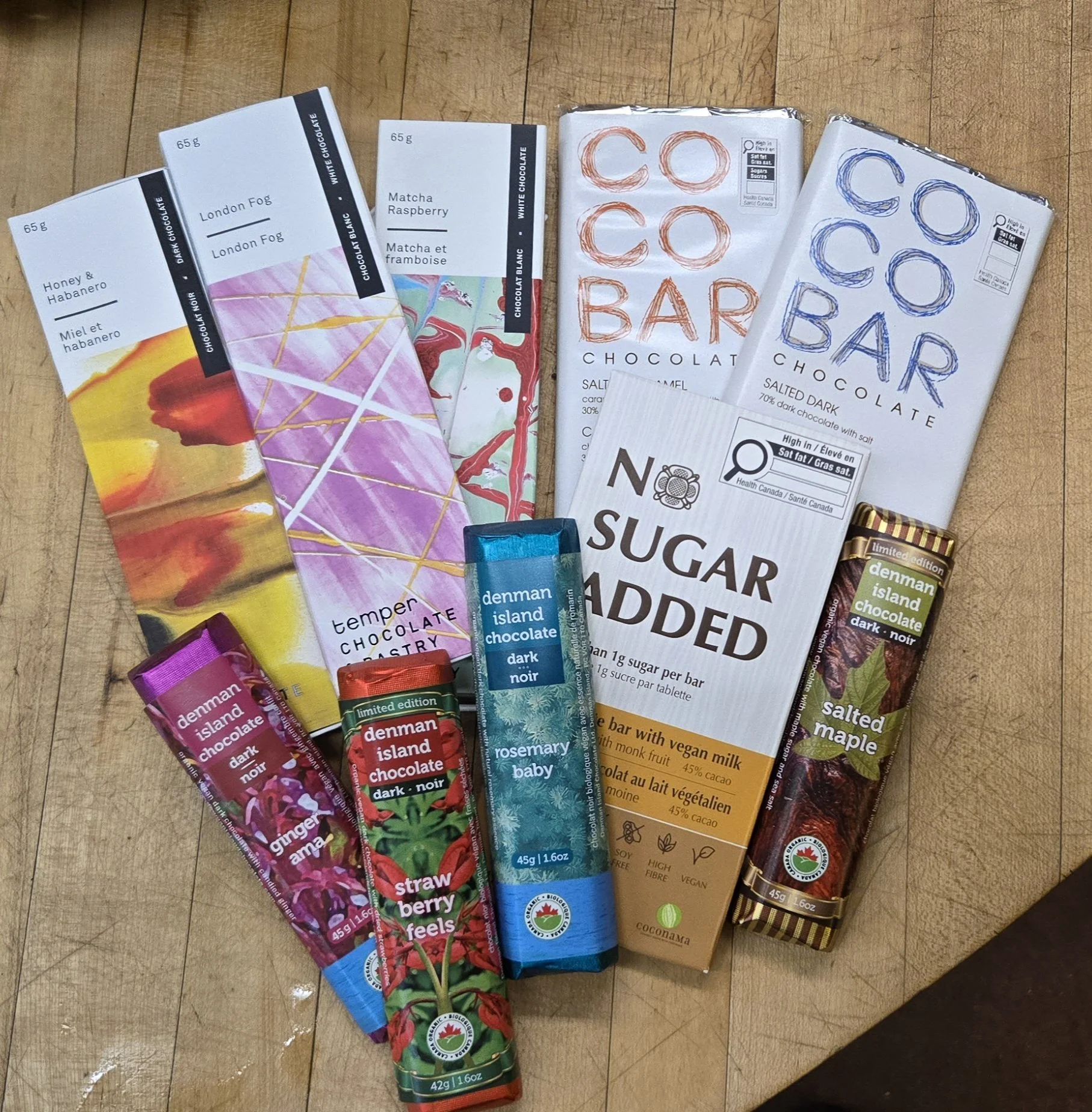 Various organic chocolate bars, including flavors like honey and habanero, London fog, matcha raspberry, salted dark chocolate maple, ginger and orange, strawberry feels, as well as smaller flavored chocolate packets such as rosemary, strawberry, and
