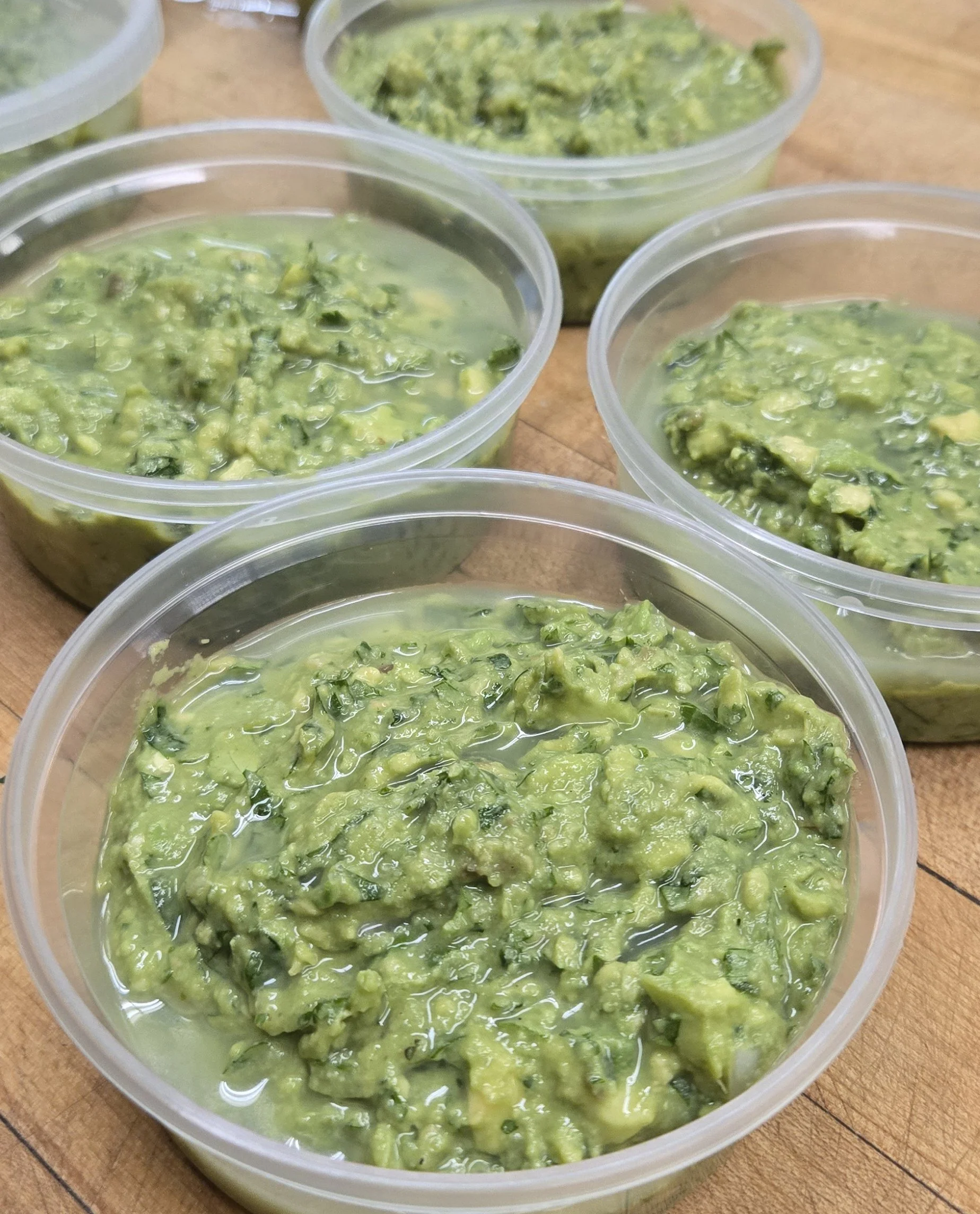 Containers of guacamole on a wooden surface.