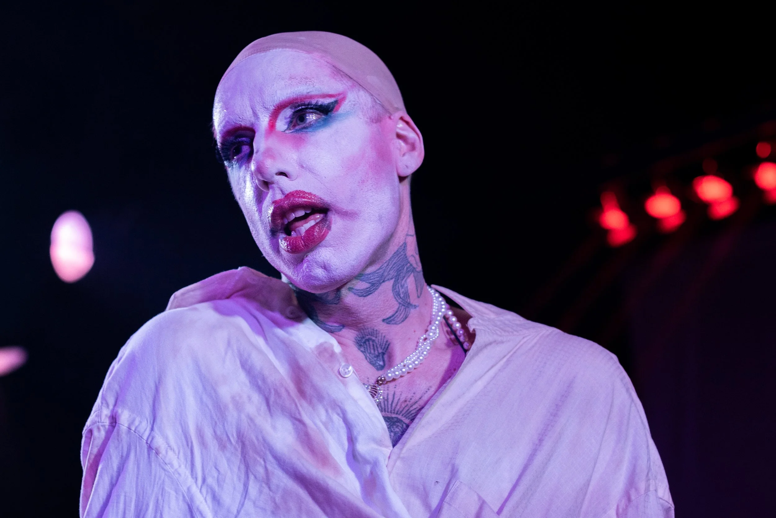 Person with theatrical makeup and tattoos performing on stage.
