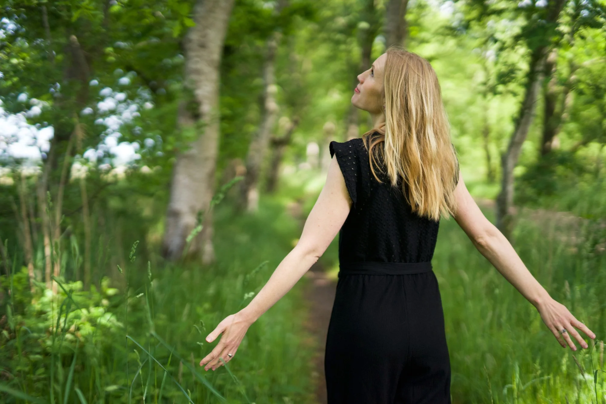 Frau schaut in den grünen Wald und öffnet die Arme