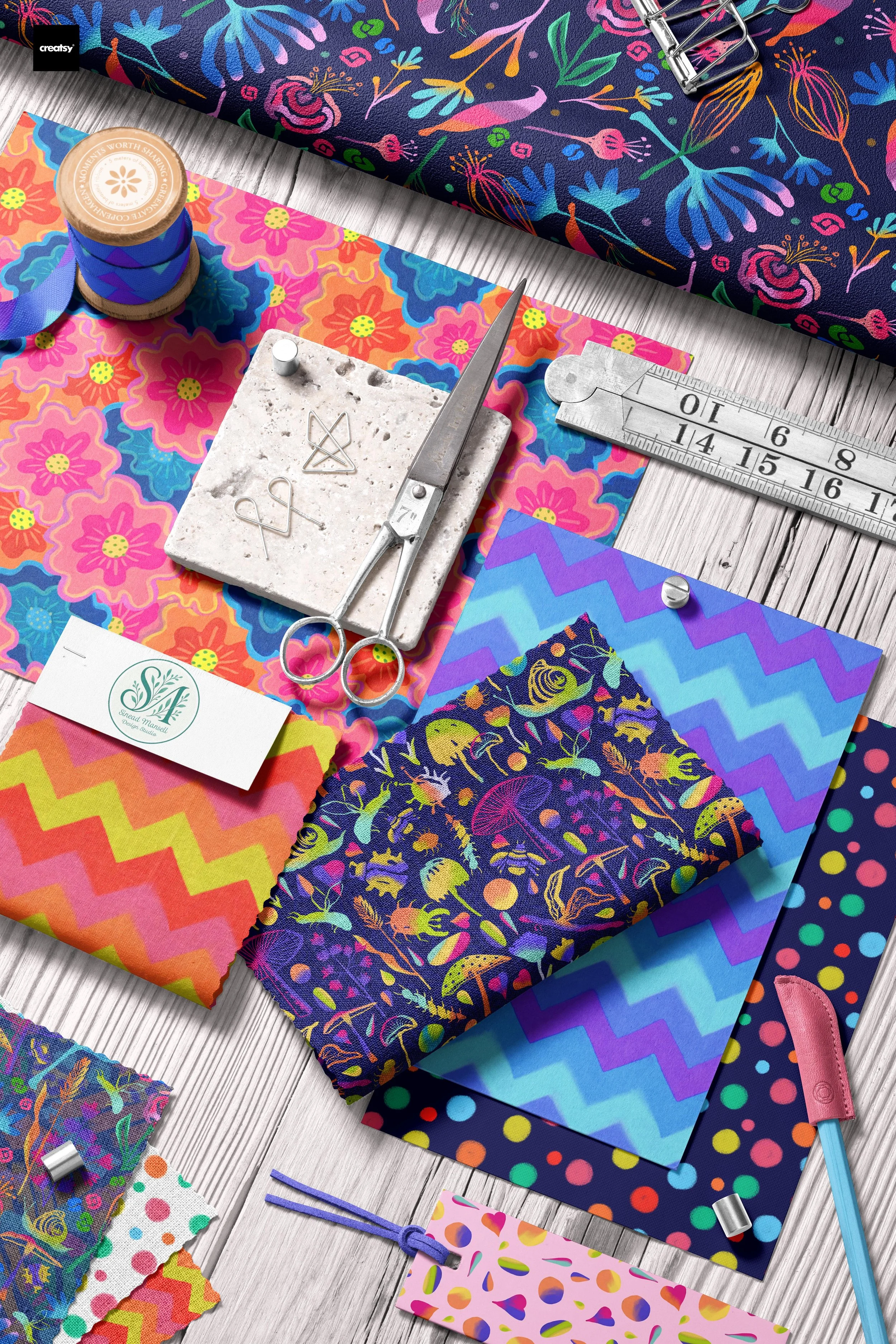 Colorful fabric swatches with floral, geometric, and abstract patterns on a white wooden surface, alongside sewing tools, tapes, and embellishments.
