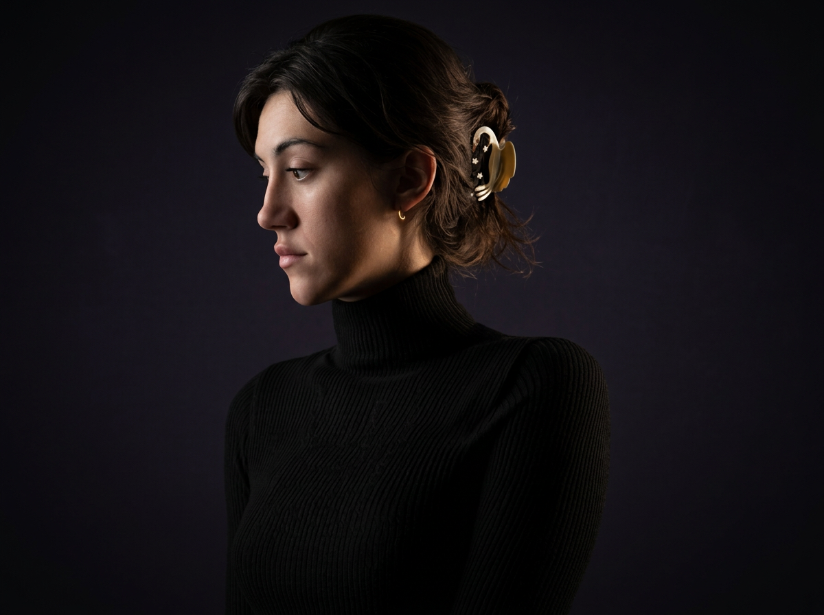 Profile of a woman with dark hair in a bun, wearing a black turtleneck sweater, and hair accessories, against a dark background.