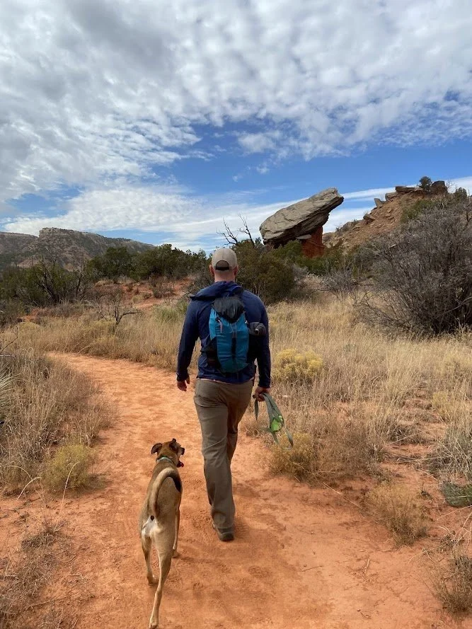 Man and brown dog hike a trail in a desert park.