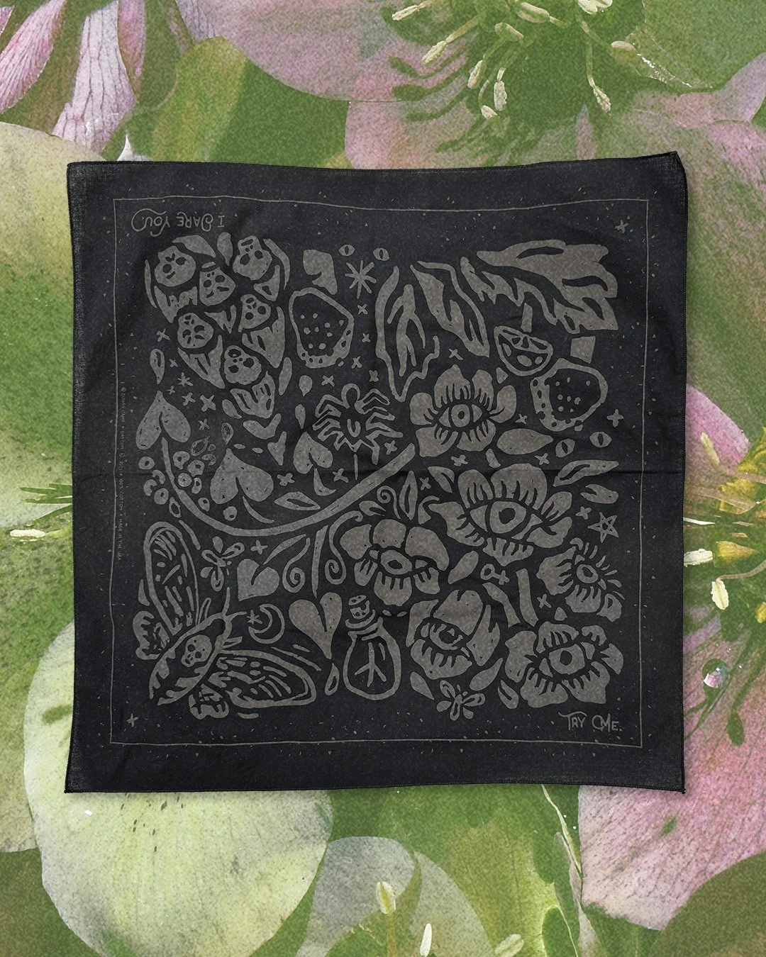Poisoner’s Garden bandana in midnight black, laid flat on a background of acid green hellebore flowers.