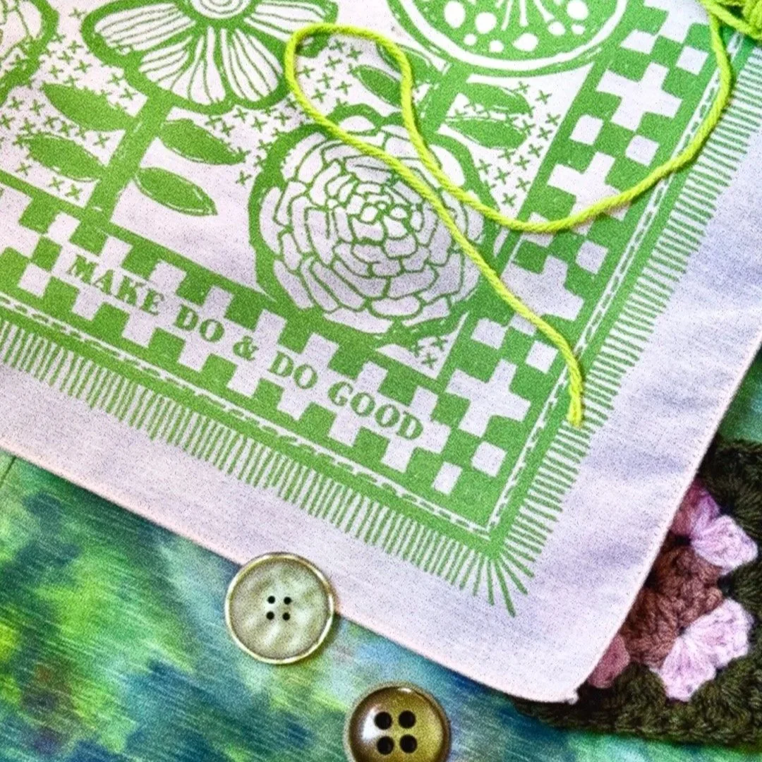Sugar Camp cream bandanna with sprout green ink features hand-drawn Scandinavian florals & stitches, reads “Make do & Do Good.” staged with with yarn and buttons
