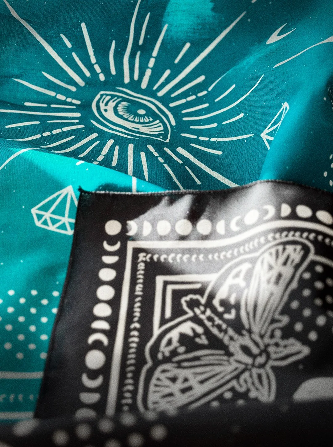 raven black & aqua Sugar Camp bandanas close up  with moth corner detail, featuring an eye in the center, and polka dots around the edge.