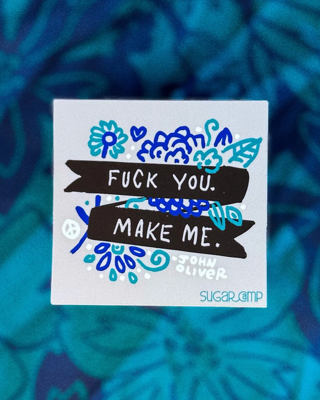 gray square sticker with hand drawn folksy flowers and 'Fuck you. Make Me' on a banner—a quote by John Oliver.