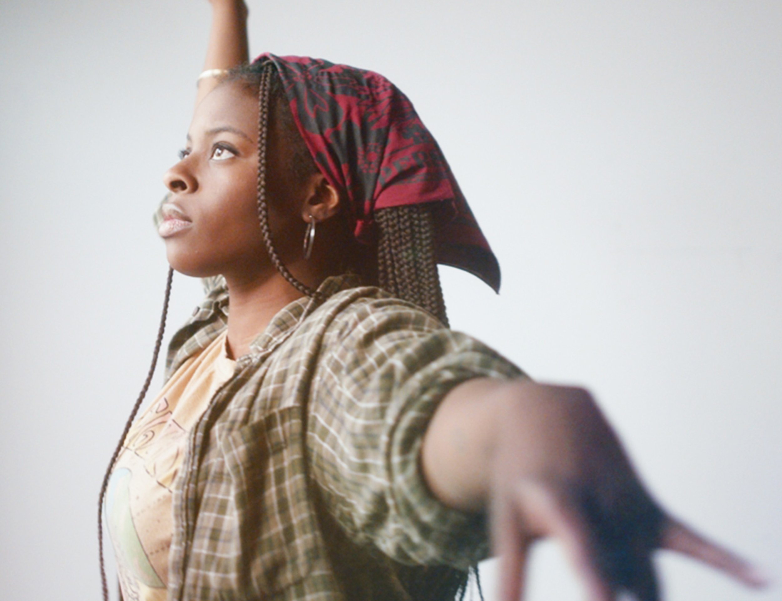 Confident young woman wearing a red floral 'RESIST' bandana inspired by feminist icons, styled as a head wrap, raising her arms in empowerment and strength.
